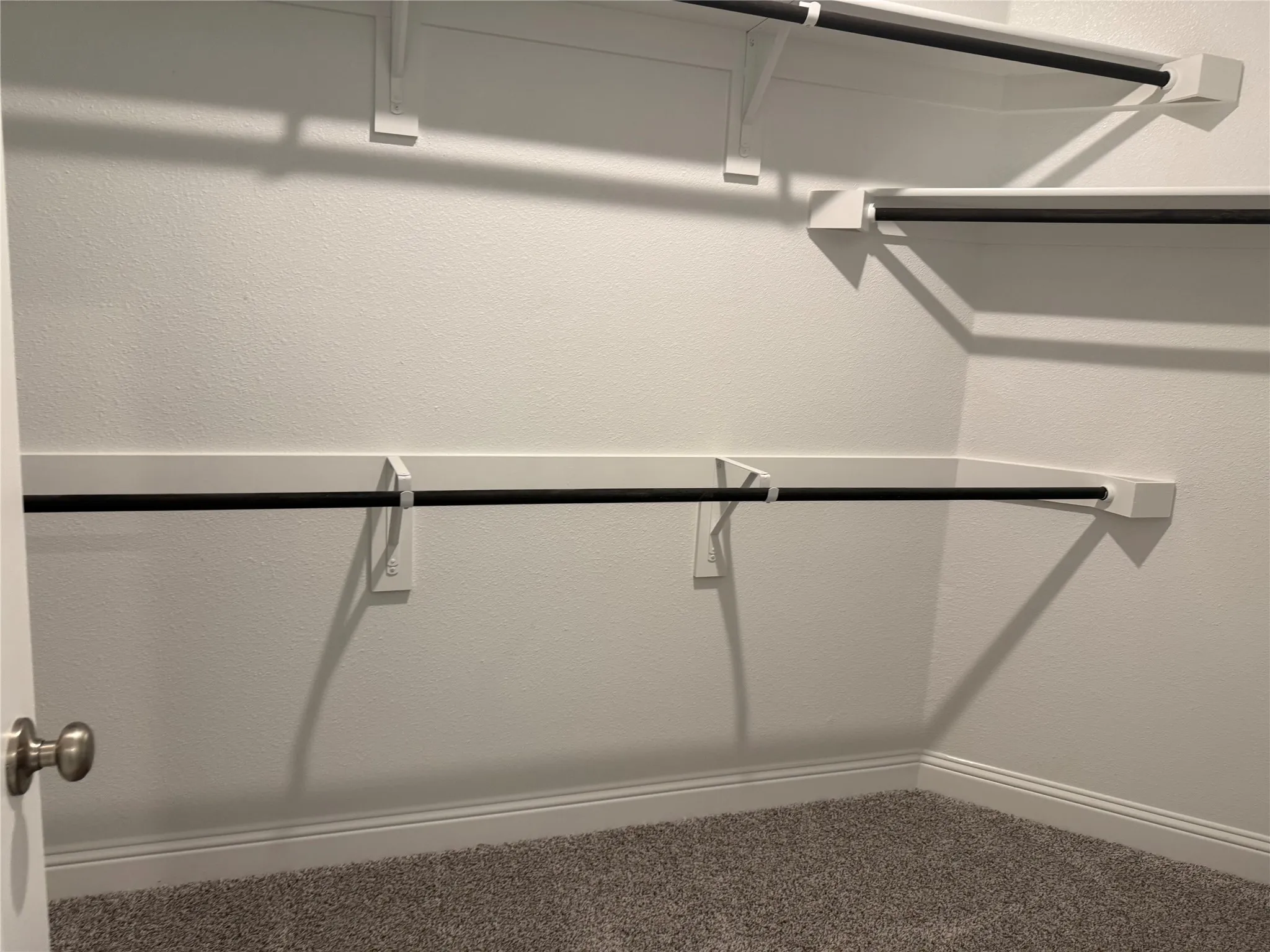 Built-in closet shelving system with multiple hanging rods, white wall finishes, and gray carpet flooring