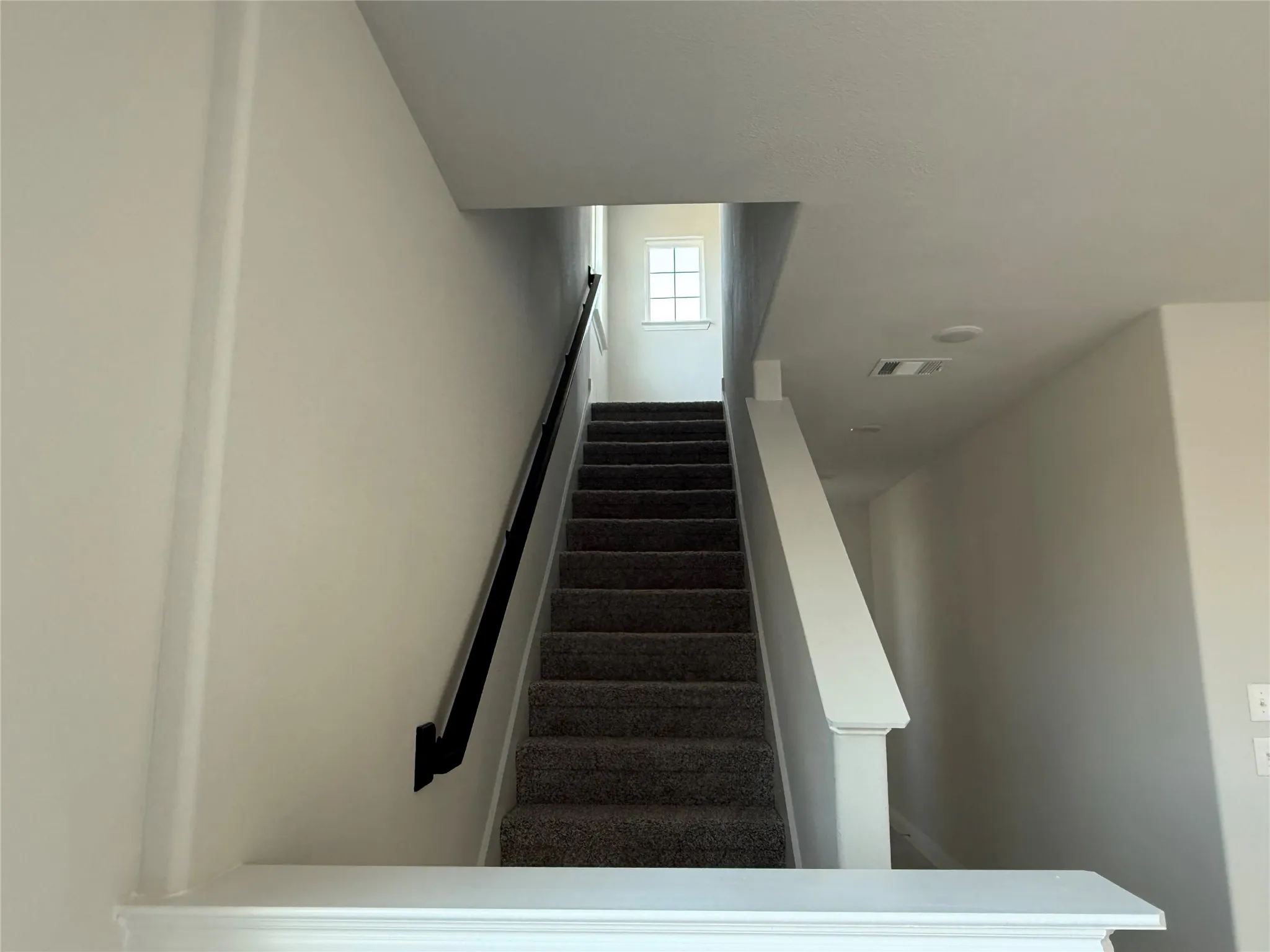 Carpeted staircase with a black handrail and white newel posts