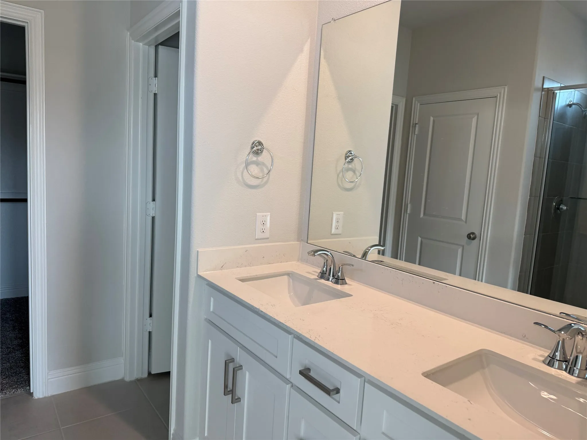Dual vanity with white cabinetry, integrated sinks, chrome fixtures, and a large wall-mounted mirror