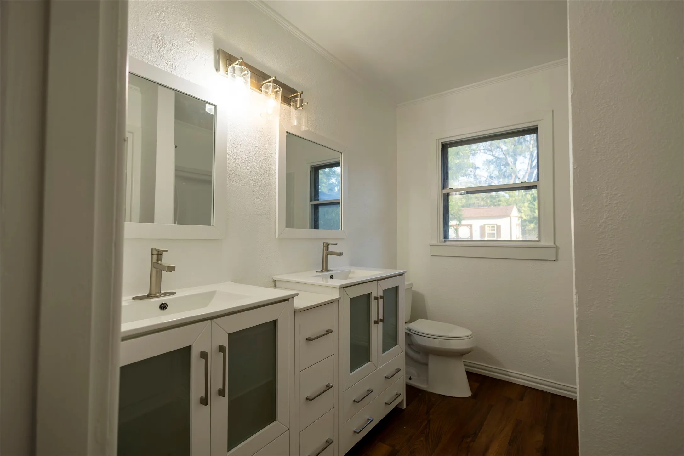 Dual vanity with integrated sinks, wood-finish flooring, and a single window