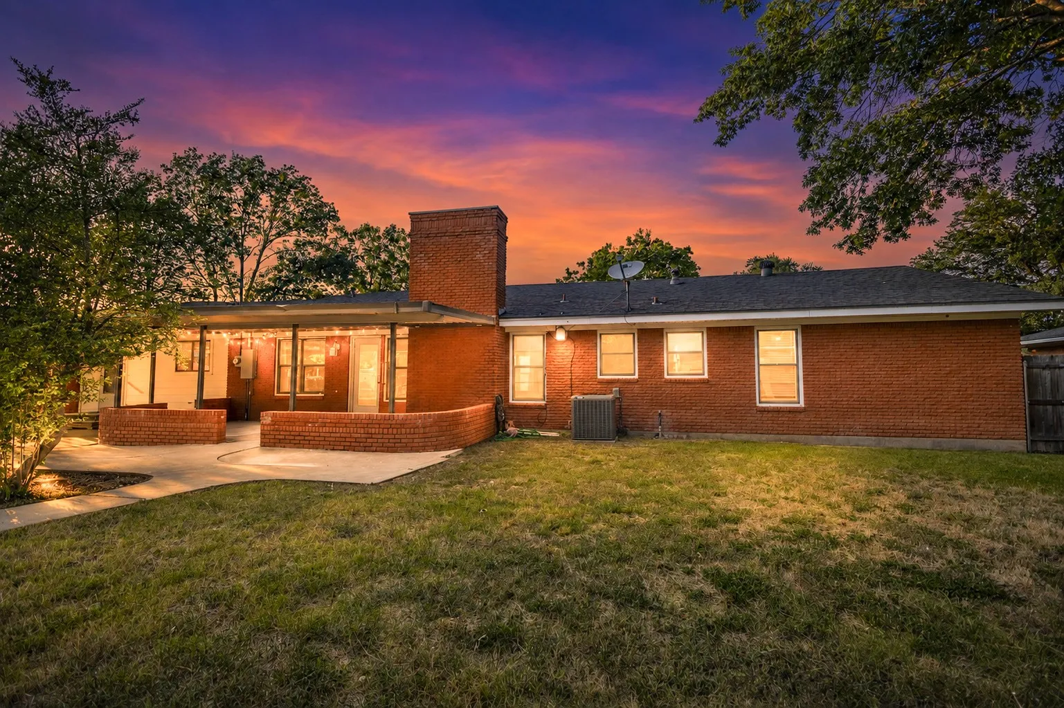 Brick exterior with a covered patio, concrete patio surface, and a brick chimney