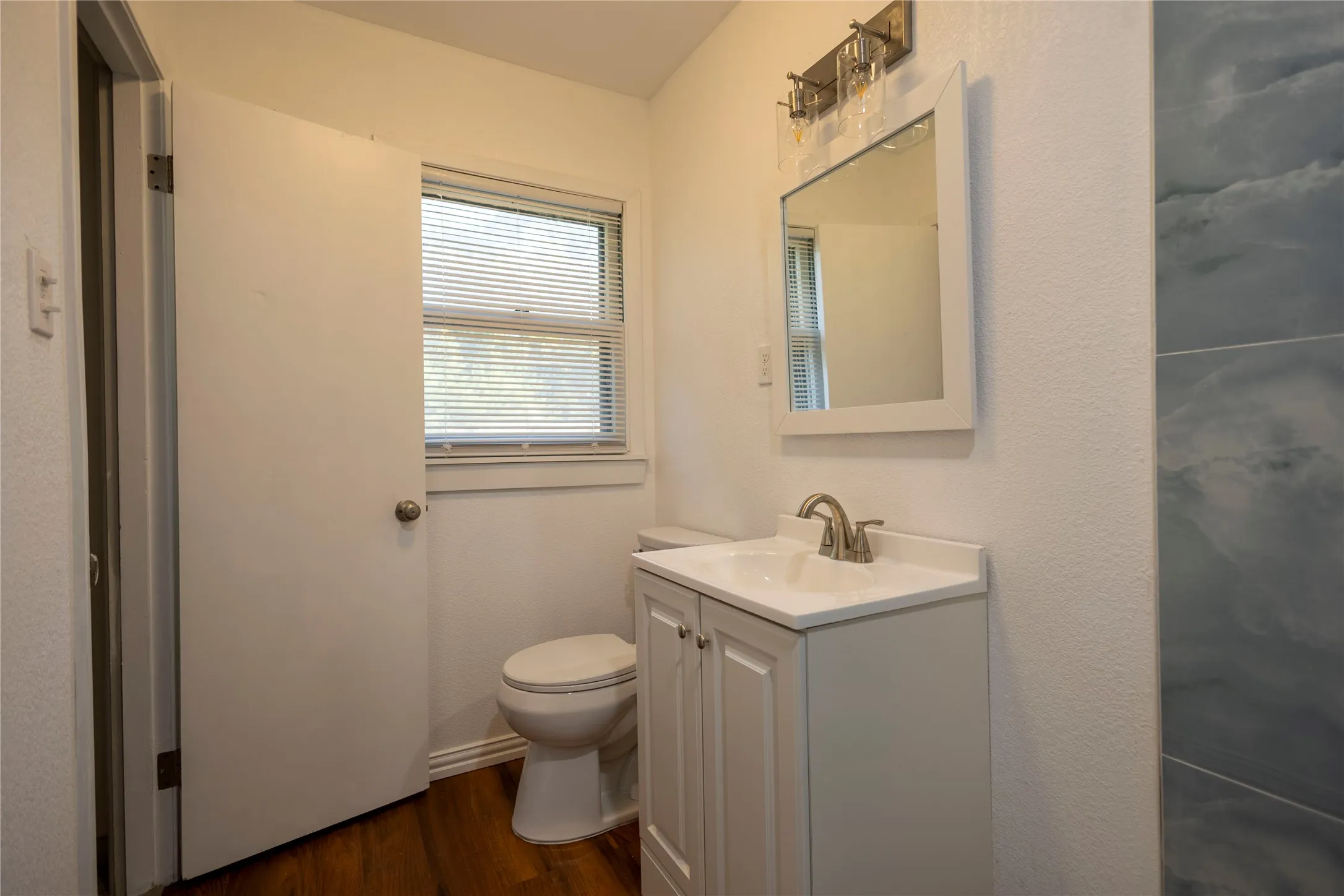 White vanity with integrated sink, brushed nickel faucet, framed mirror, and wood-finish flooring
