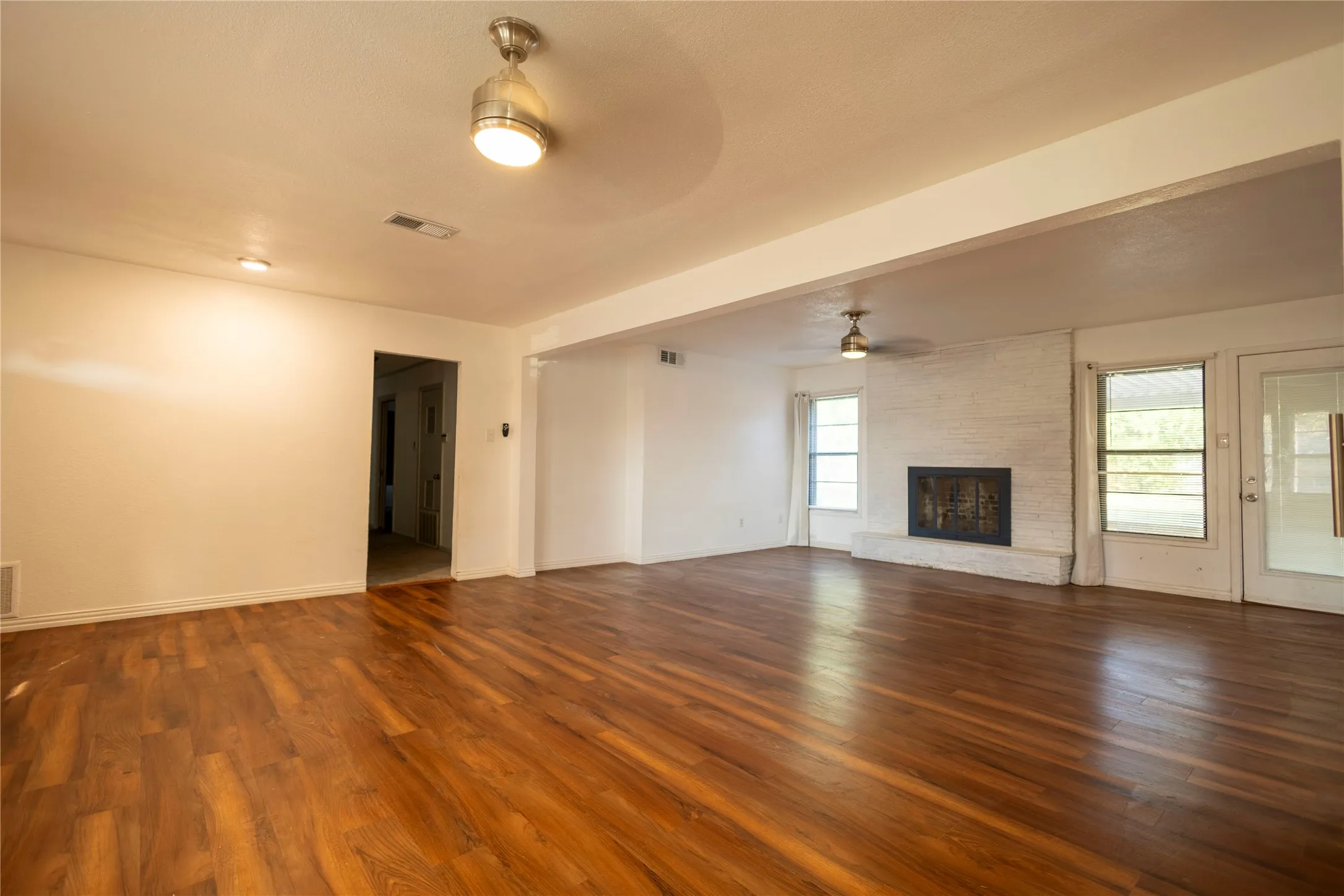 Spacious room with wood-finish flooring, a painted brick fireplace, and multiple windows