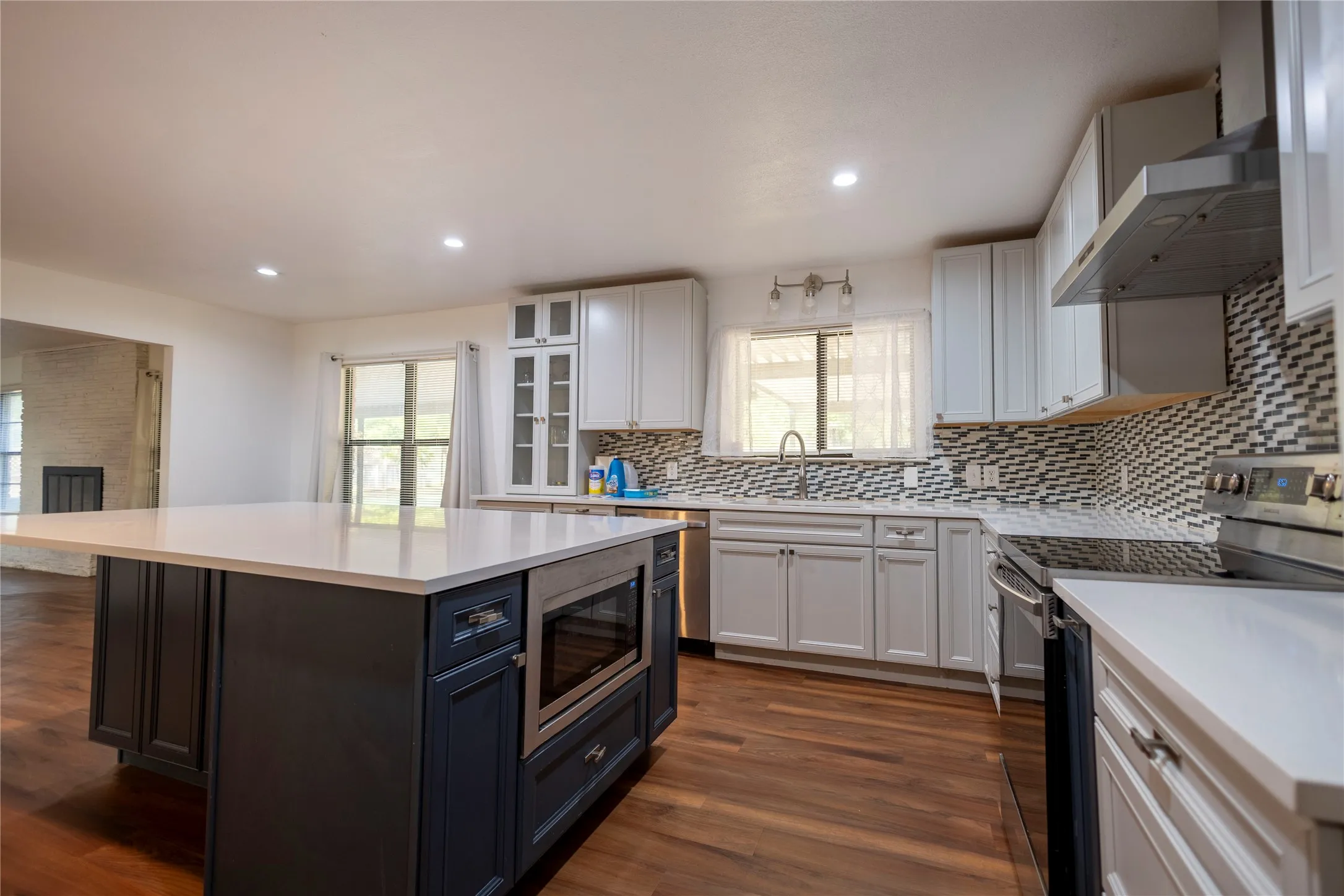 Island kitchen featuring wood-finish flooring, white cabinetry, a built-in microwave, and a tiled backsplash