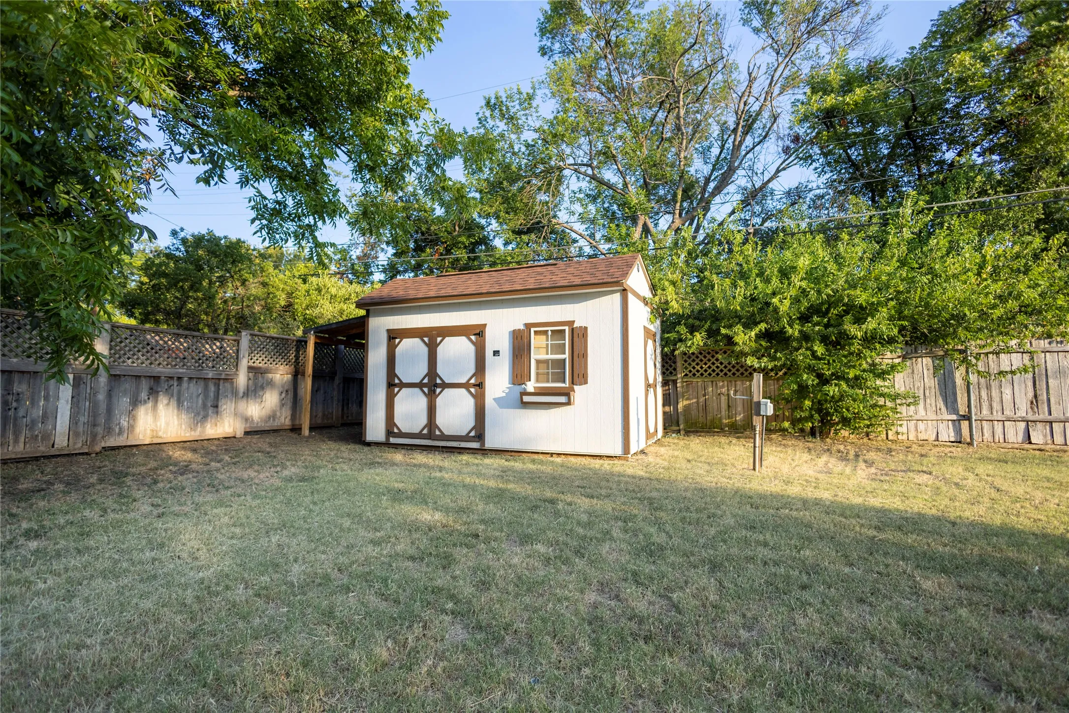 Expansive grassy yard featuring a shed with a brown shingle roof, wood-look shutters, a single-paned window, and a covered side entry