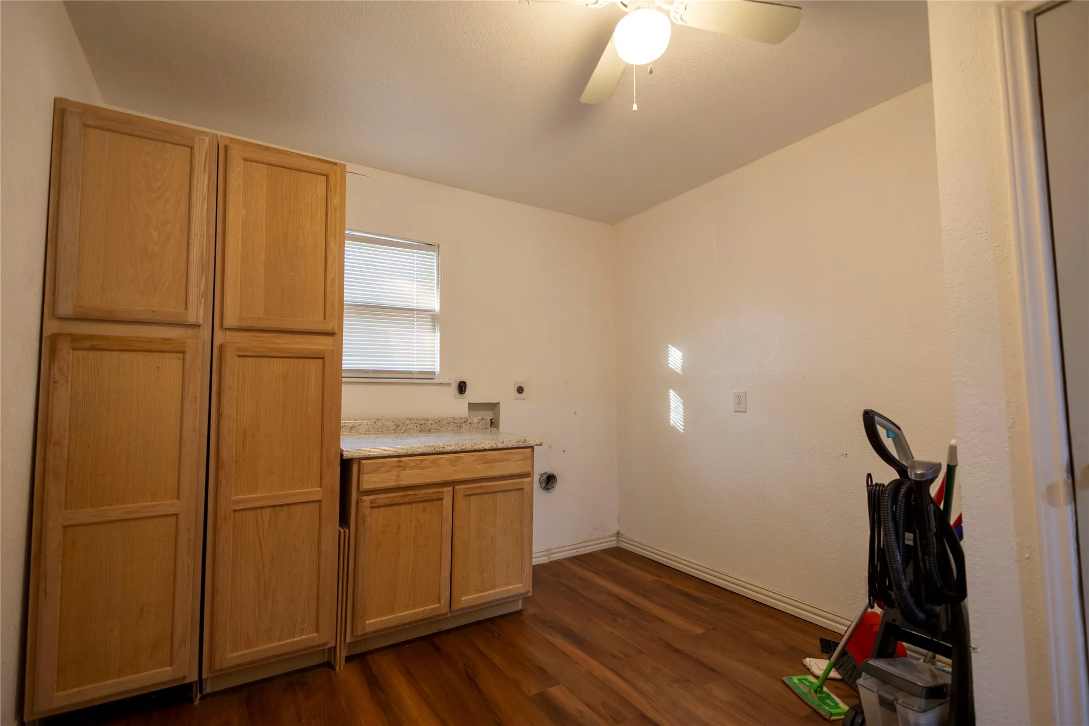 Laundry area featuring wood-finish flooring, built-in cabinetry, a window with blinds, and a ceiling fan