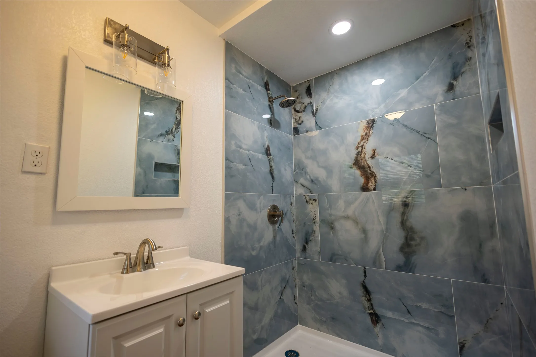 Shower with blue-toned stone-patterned tile, integrated shower niche, and a rain shower head