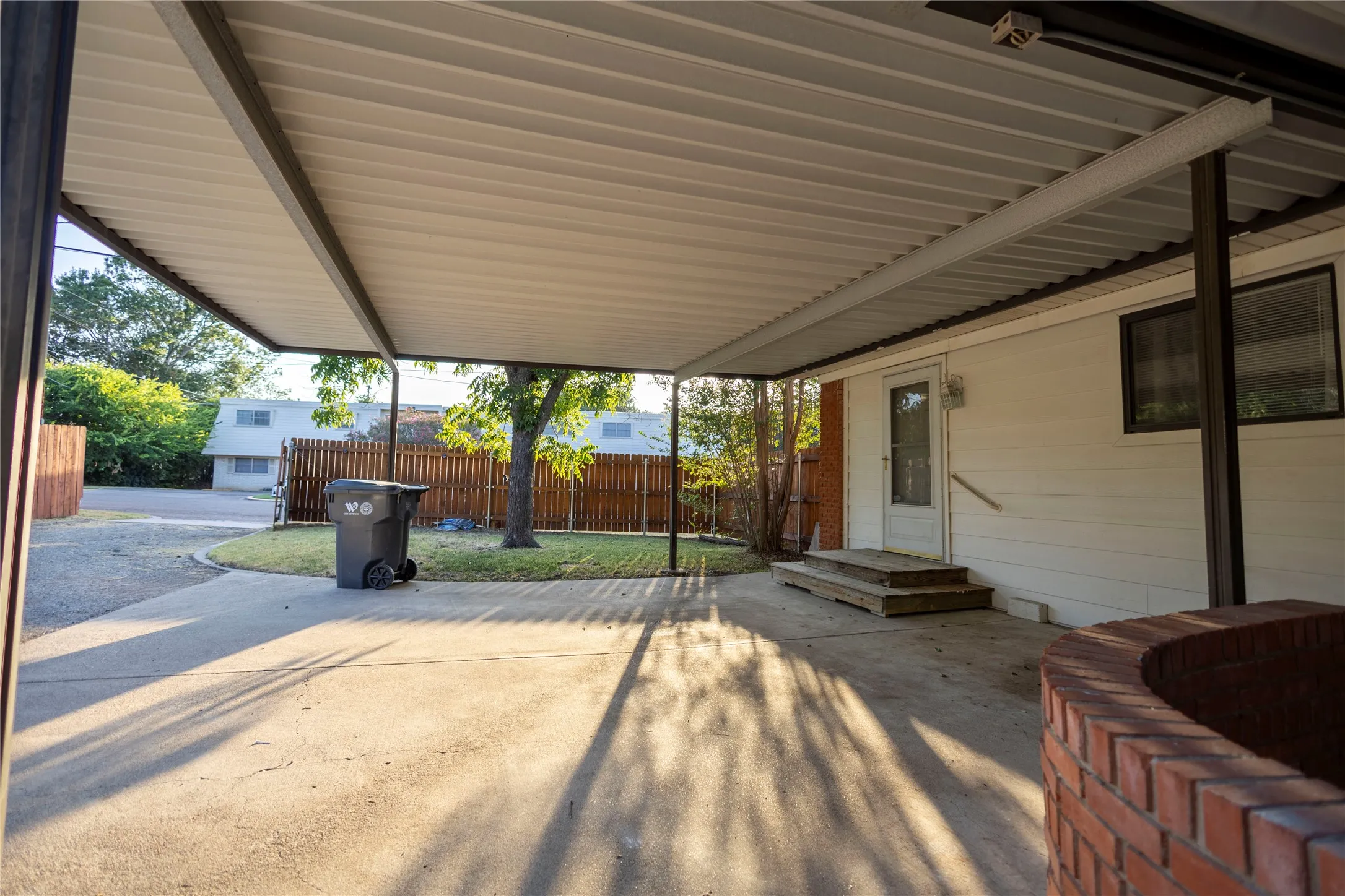 Covered carport with concrete paving, wood fencing, and a brick planter