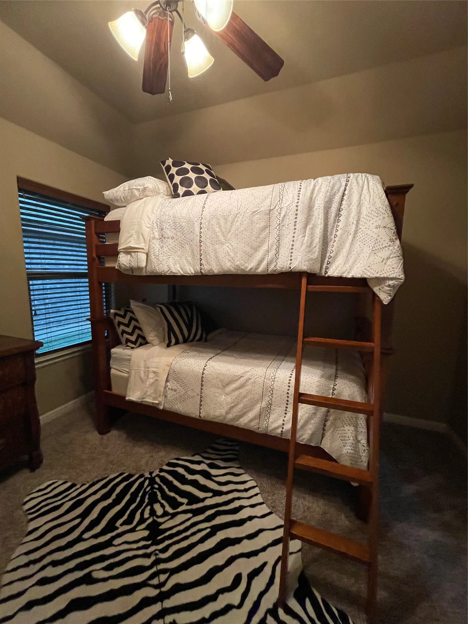 Room featuring vaulted ceiling, flush-mount ceiling fan with light kit, textured carpeting, and window with horizontal blinds