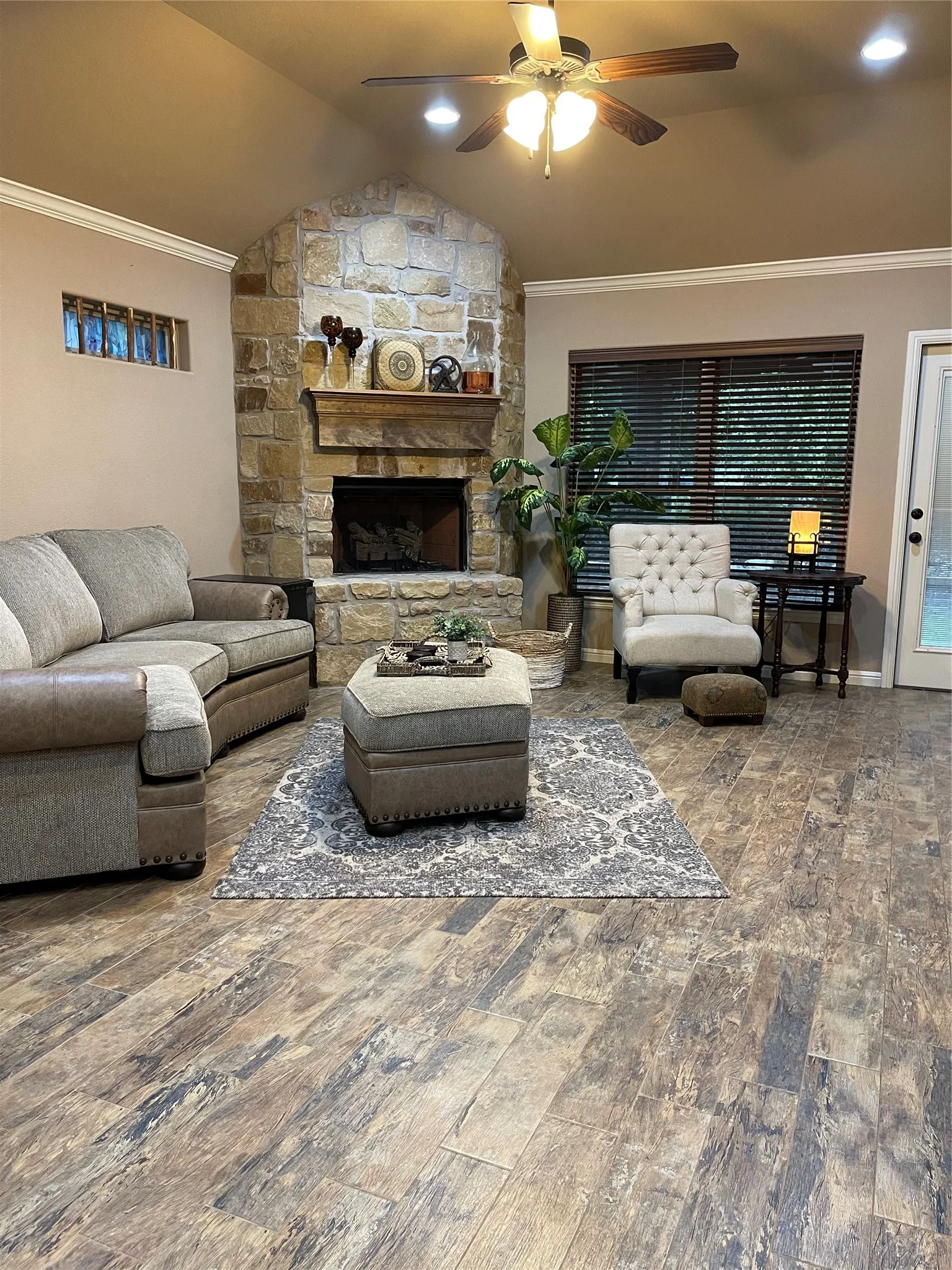 Stone-clad fireplace with a wood mantle, wood-finish flooring, vaulted ceiling, and a ceiling fan with integrated lighting