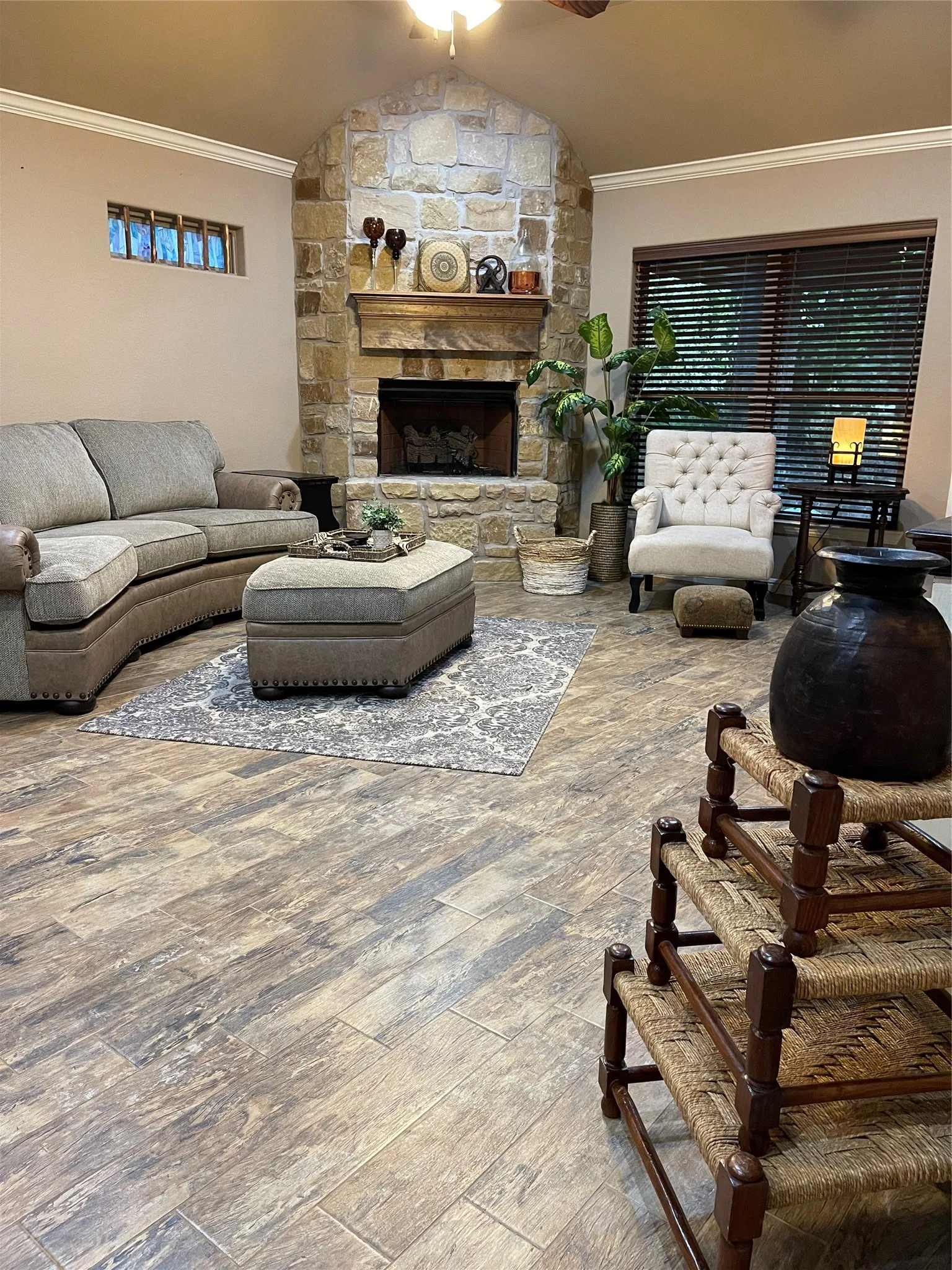 Stone-clad fireplace with a wood mantel, wood-finish flooring, and crown molding