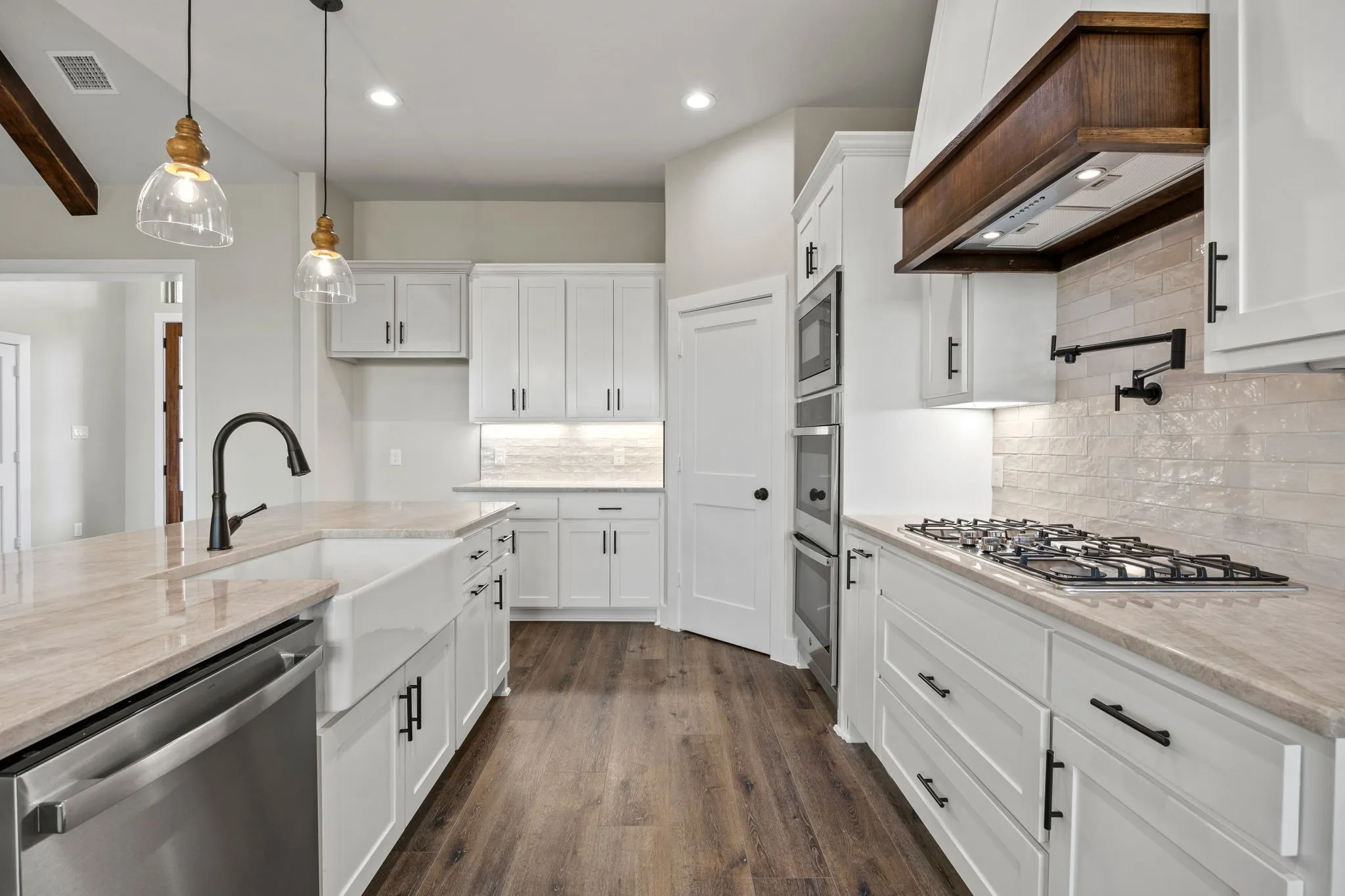 Modern kitchen featuring white shaker cabinetry, light-toned countertops, a farmhouse sink with a gooseneck faucet, and stainless steel appliances, all complemented by wood-finish flooring