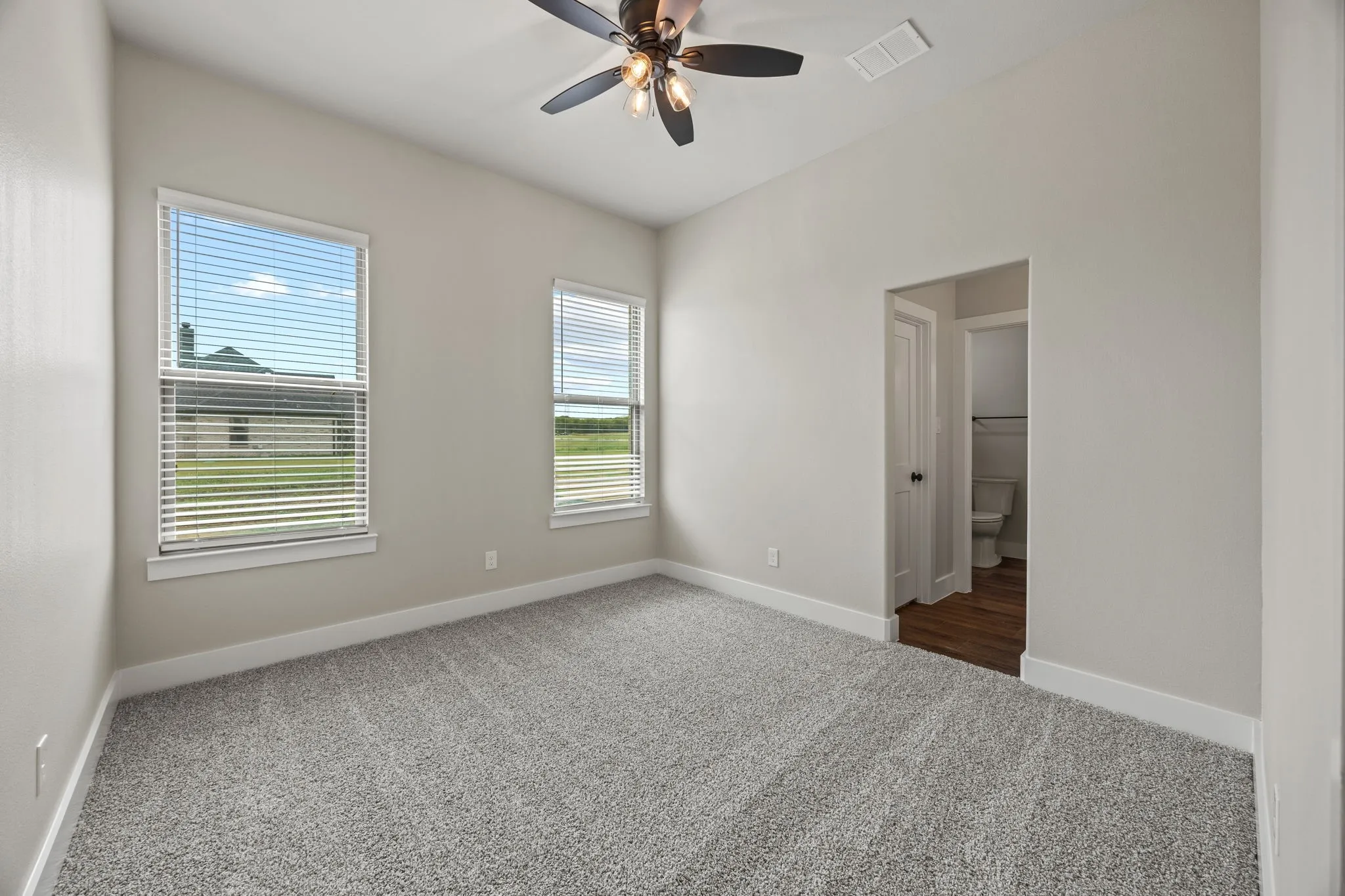 Vaulted ceiling with an attached ceiling fan, dual windows, gray carpeting, and a doorway leading to a separate space