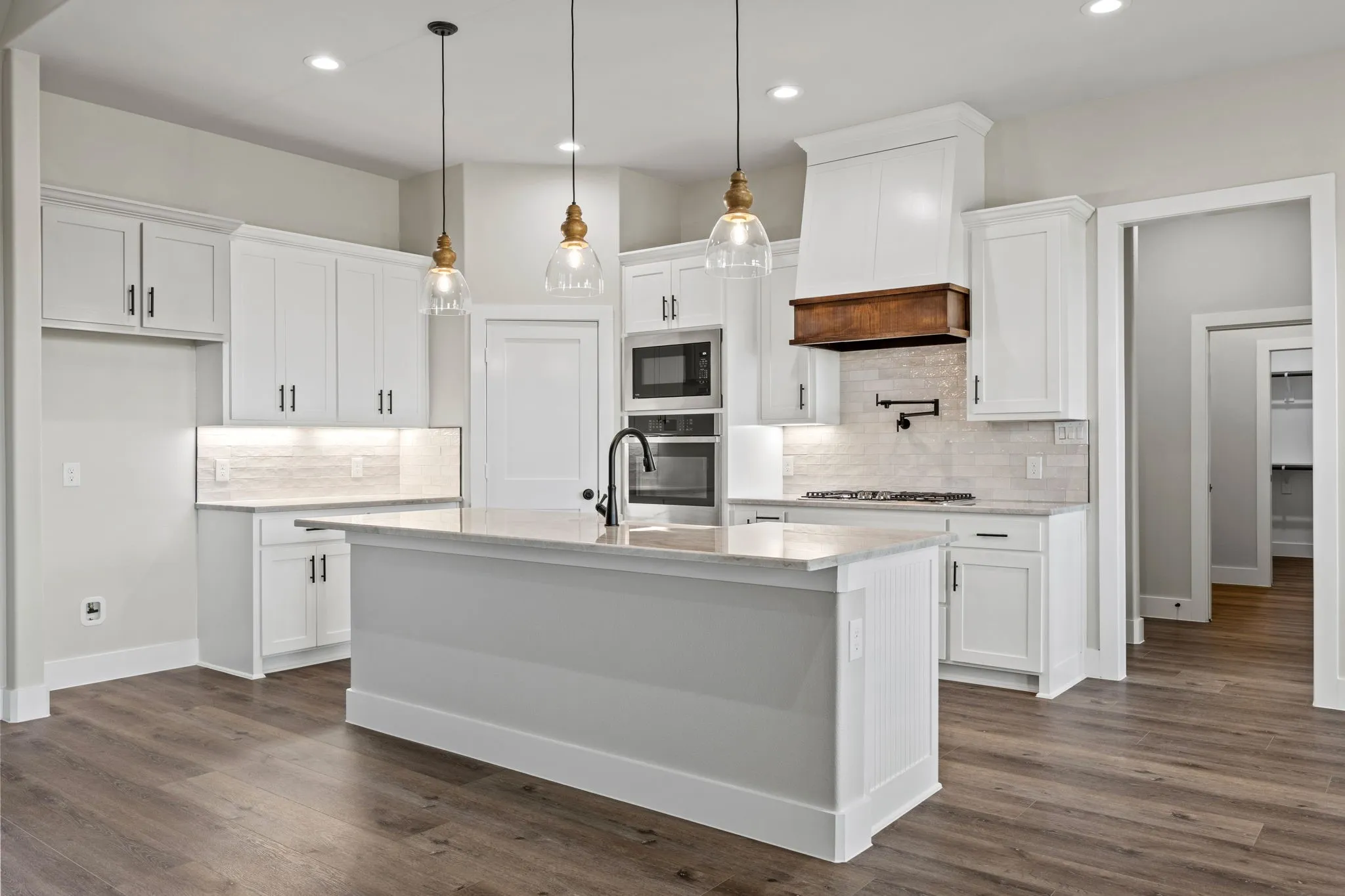 Kitchen featuring white cabinetry, built-in stainless steel appliances, a center island with a sink, wood-finish flooring, and pendant lighting