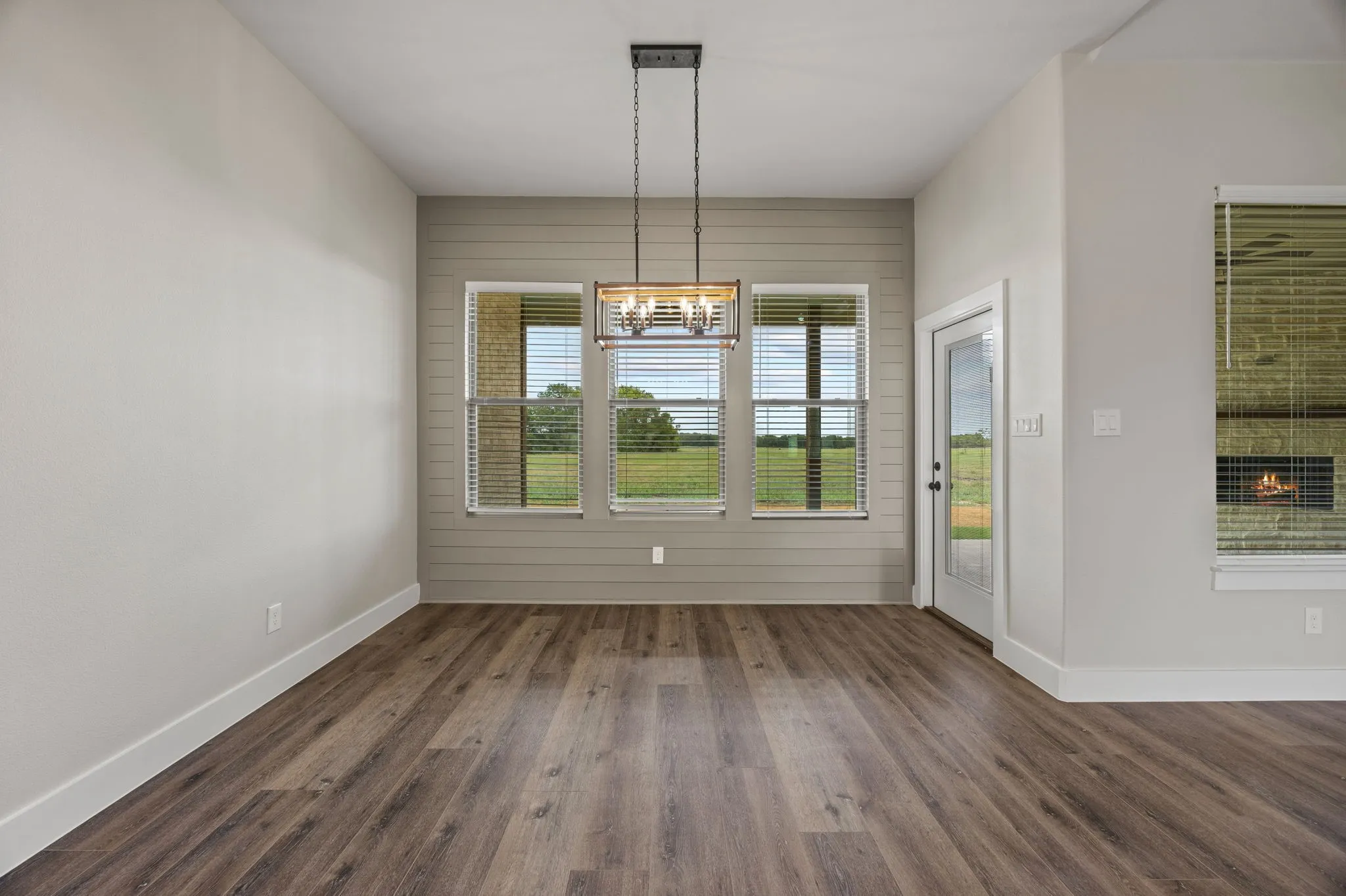 Wood-finish flooring with crisp white baseboards, featuring a contemporary chandelier and multiple windows