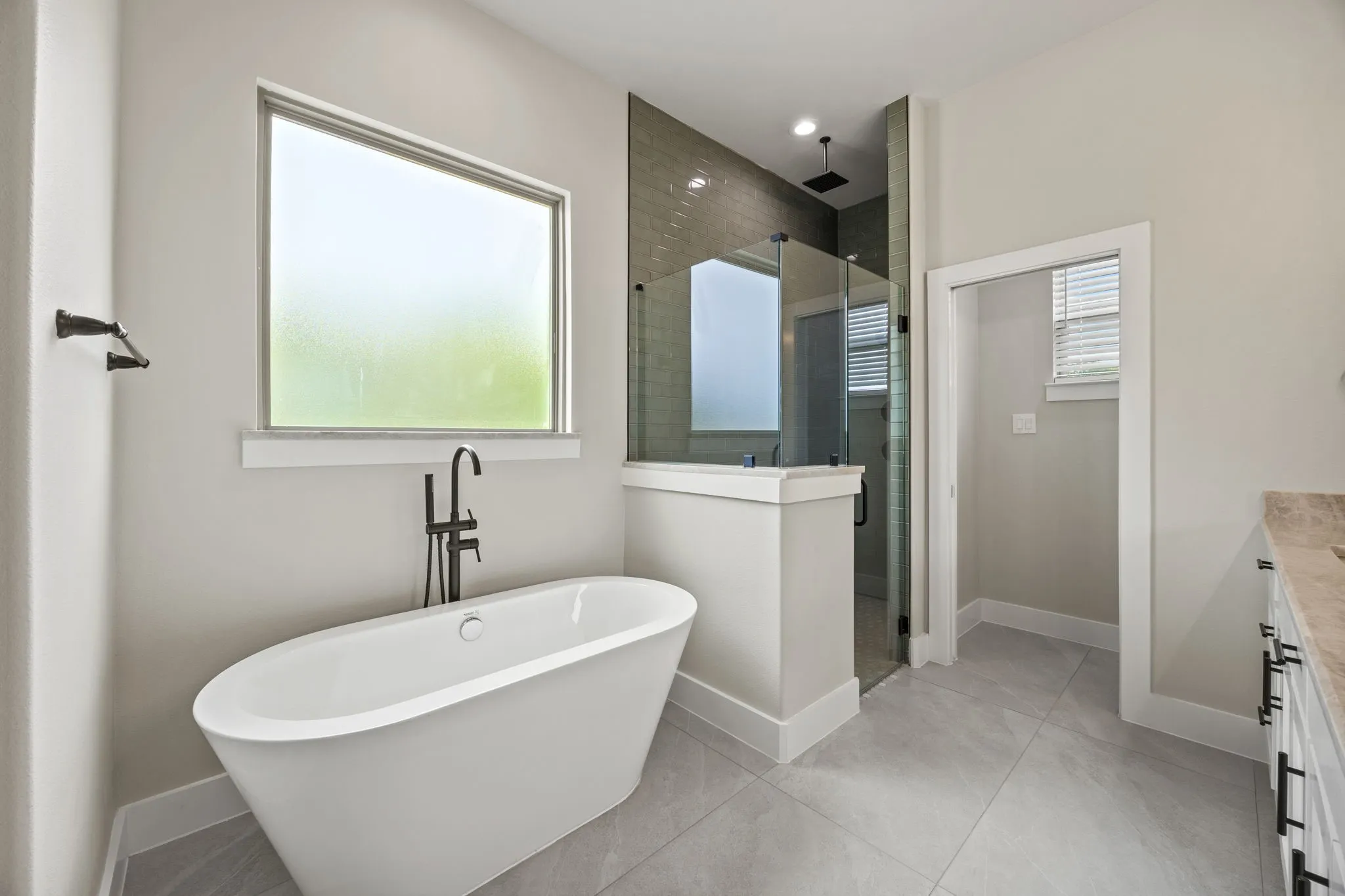 Freestanding soaking tub with a matte black floor-mounted faucet, oversized walk-in shower with glass enclosure, tiled shower walls, and light-toned tile flooring