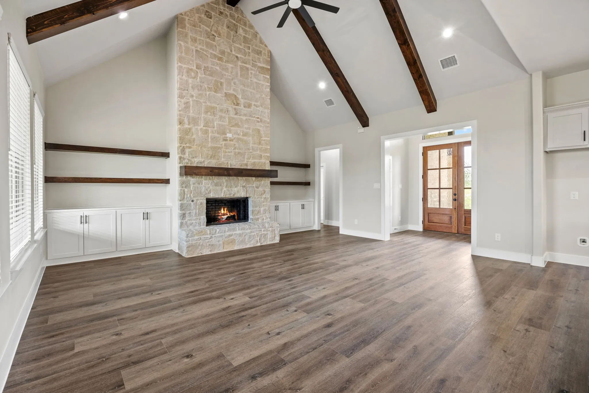 Vaulted ceiling with exposed wood beams, stone-clad fireplace, wood-finish flooring, built-in cabinetry, and a paneled wood entry door with glass inserts