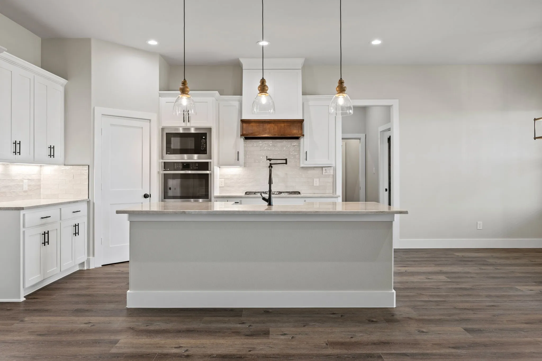 Bright kitchen featuring a central island, wood-finish flooring, white cabinetry, integrated stainless steel appliances, and pendant lighting