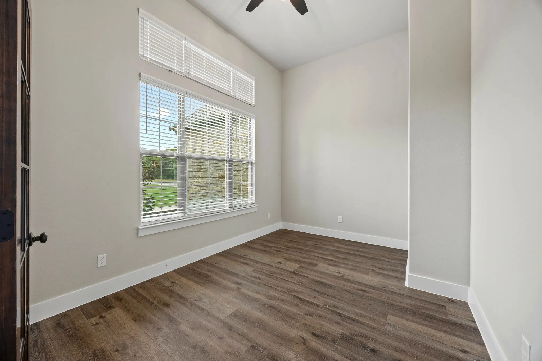 Wood-finish flooring, high ceilings, large windows with upper transom windows, and a dark wood-paneled door