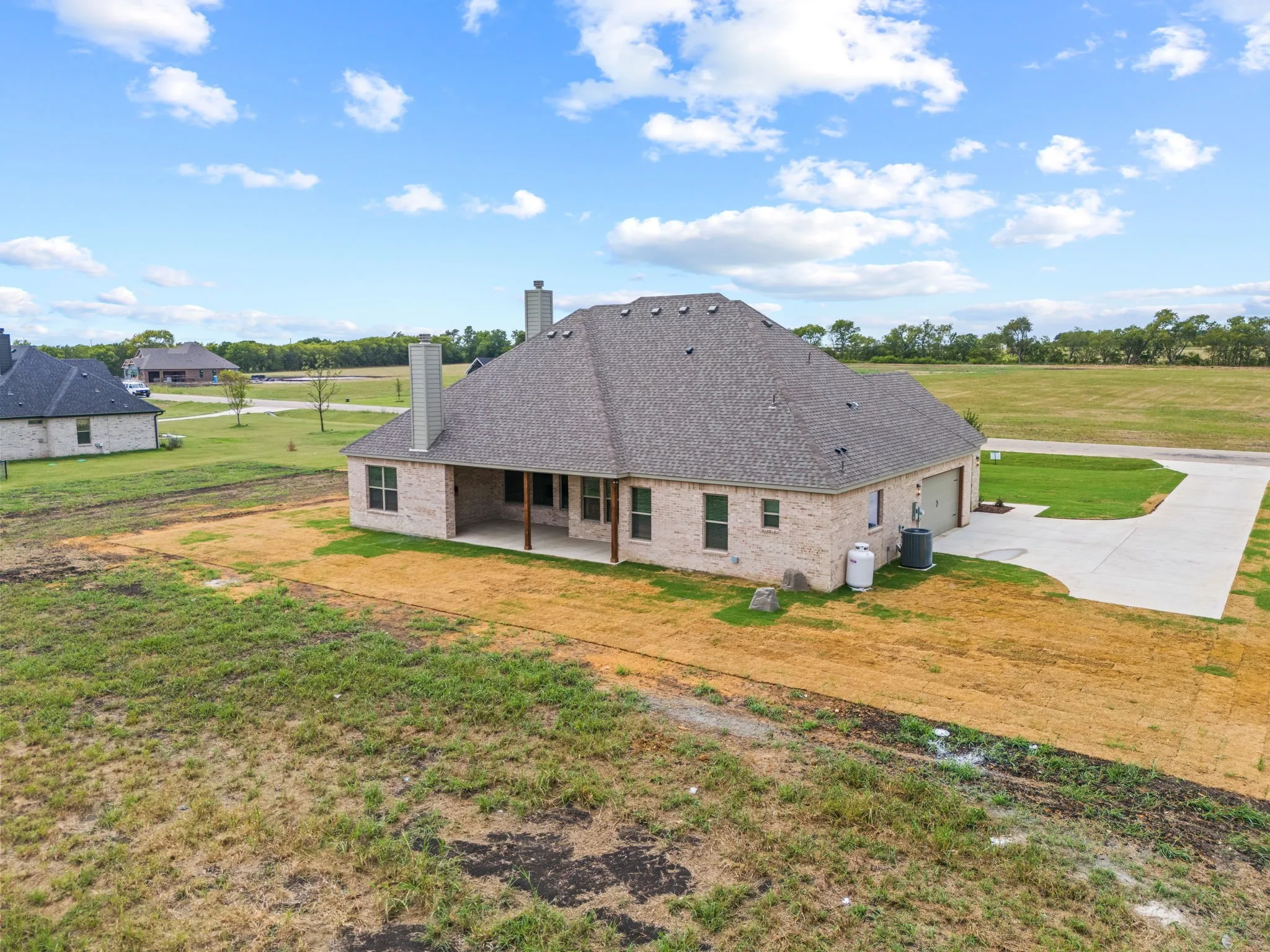 Brick exterior with a shingle roof, offering a covered patio, double garage door, and a concrete driveway