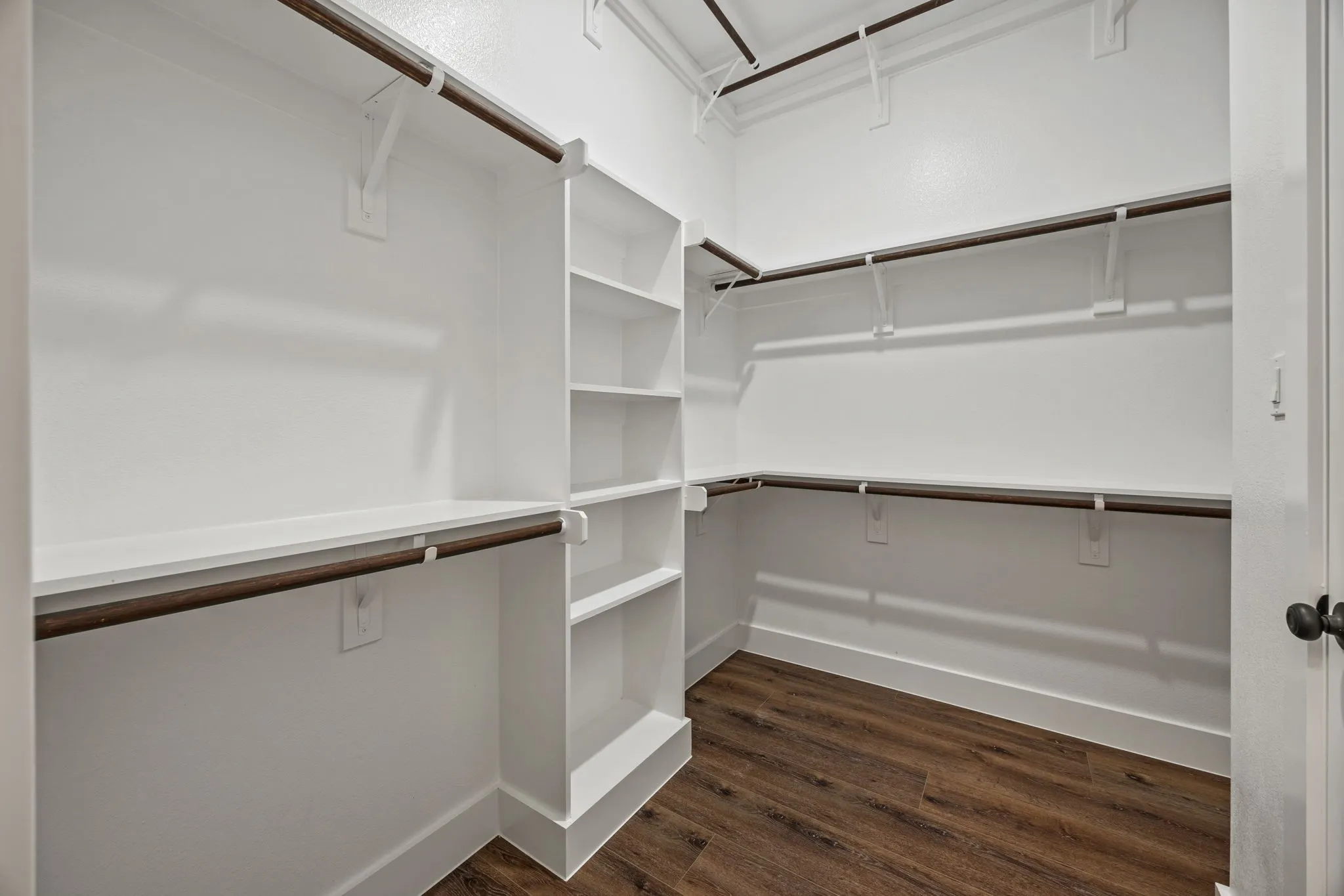 Walk-in closet featuring built-in shelving, multiple hanging rods, and wood-finish flooring