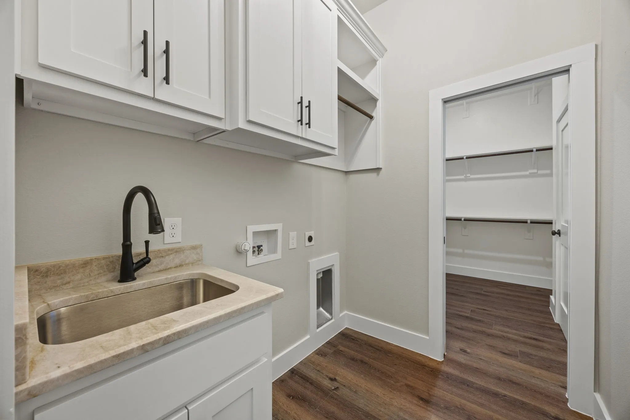 White shaker cabinetry, stainless steel utility sink, black gooseneck faucet, light-toned countertop, and wood-finish flooring