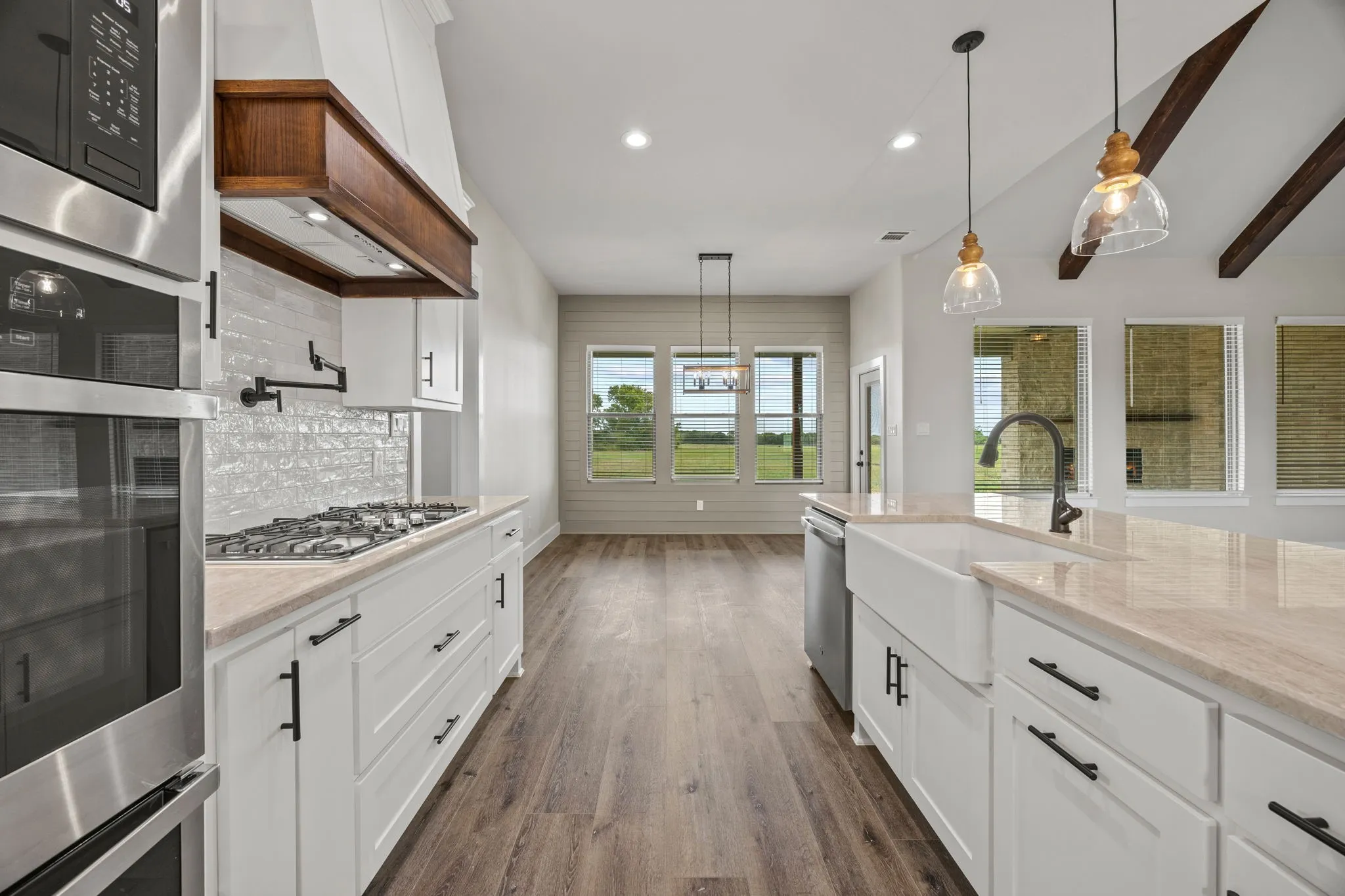 Gourmet kitchen featuring a built-in oven, gas range, wood-finish flooring, white cabinetry with dark hardware, and an apron-front sink
