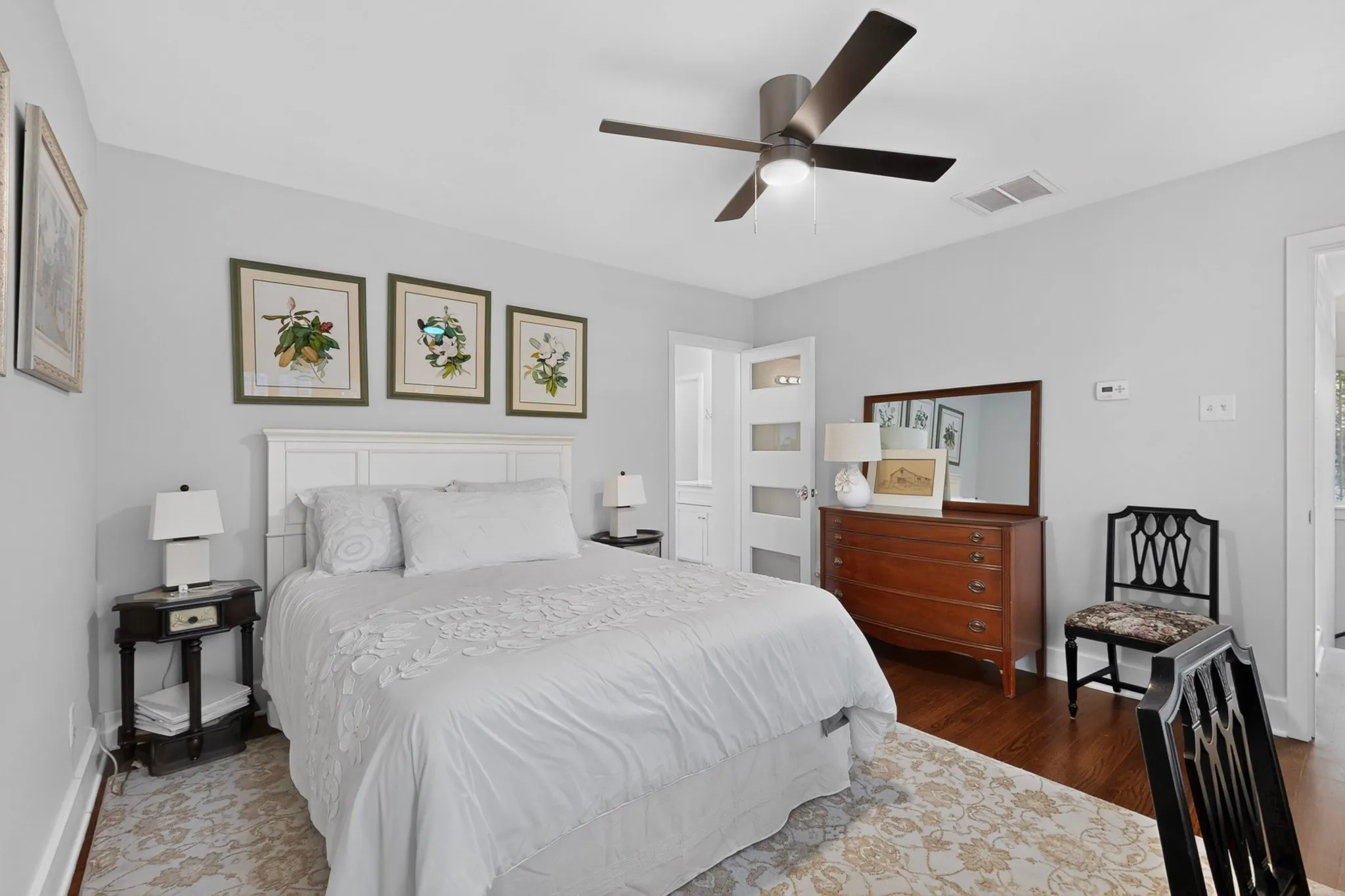 White paneled headboard, ceiling fan with integrated lighting, wood-finish flooring, and light gray wall paint