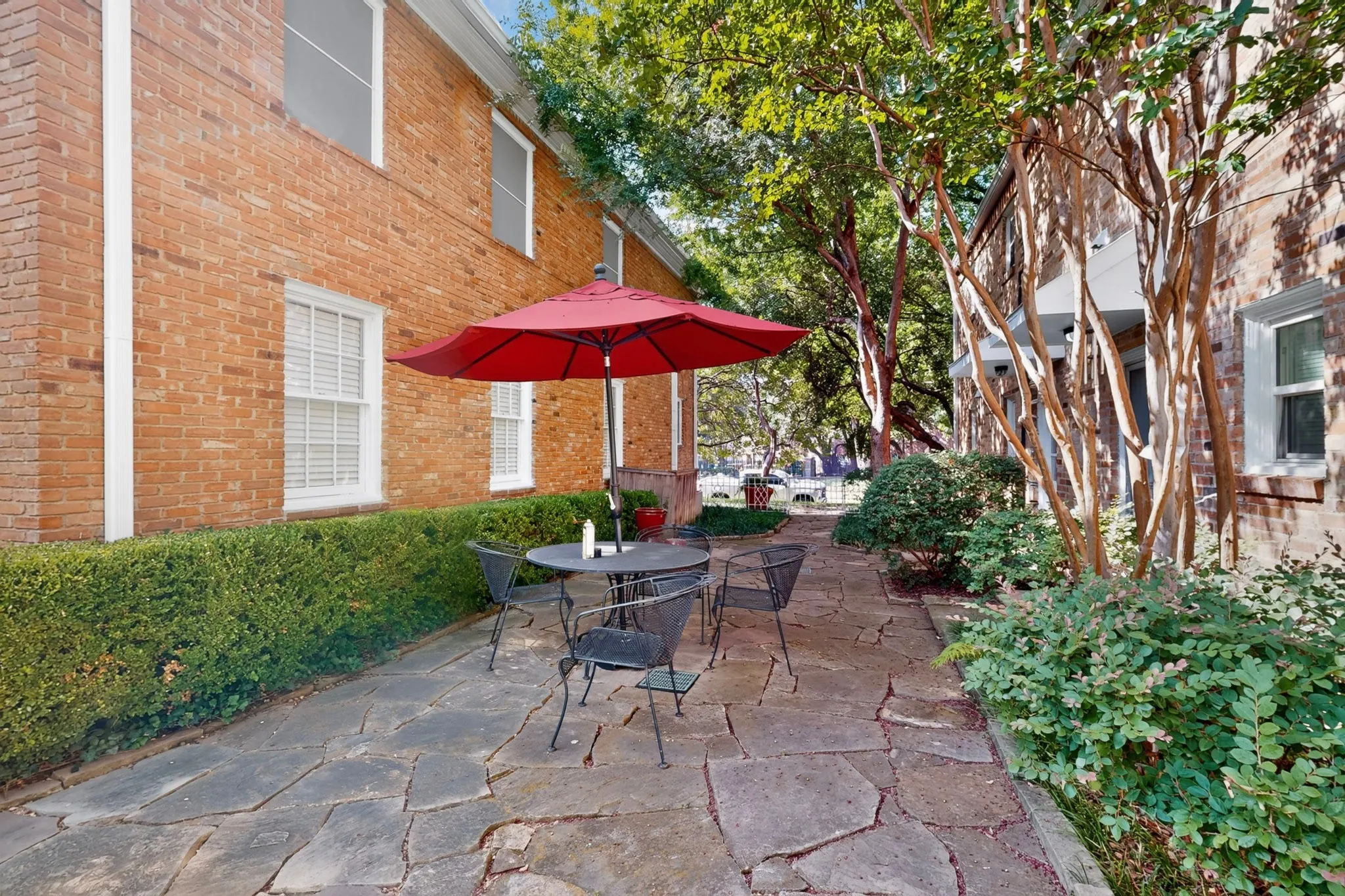 Flagstone patio bordered by mature hedges, featuring a classic brick exterior and established trees