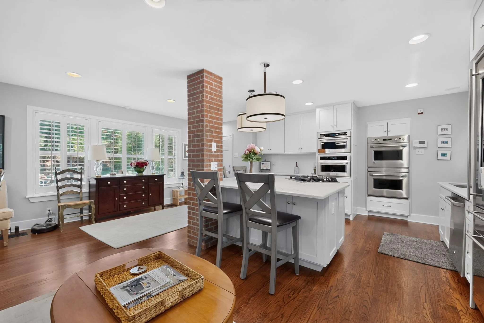Hardwood flooring throughout, white shaker cabinetry, stainless steel double ovens, recessed lighting, and a brick accent column