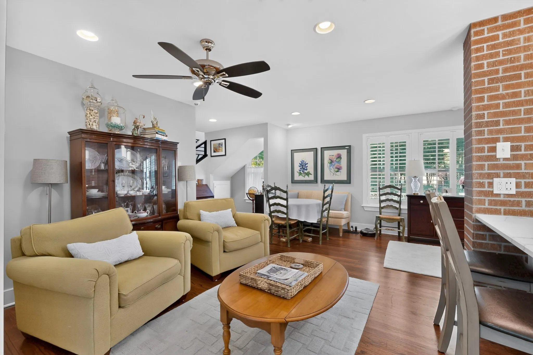 Wood-finish flooring, recessed lighting, ceiling fan, white window shutters, and a brick accent wall