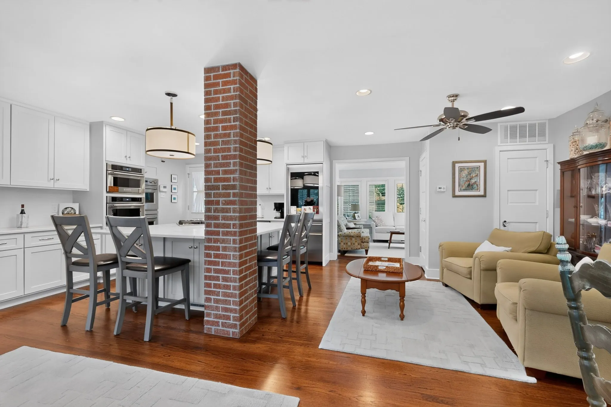 Kitchen island with seating, white cabinetry, integrated stainless steel appliances, brick column feature, and wood-finish flooring