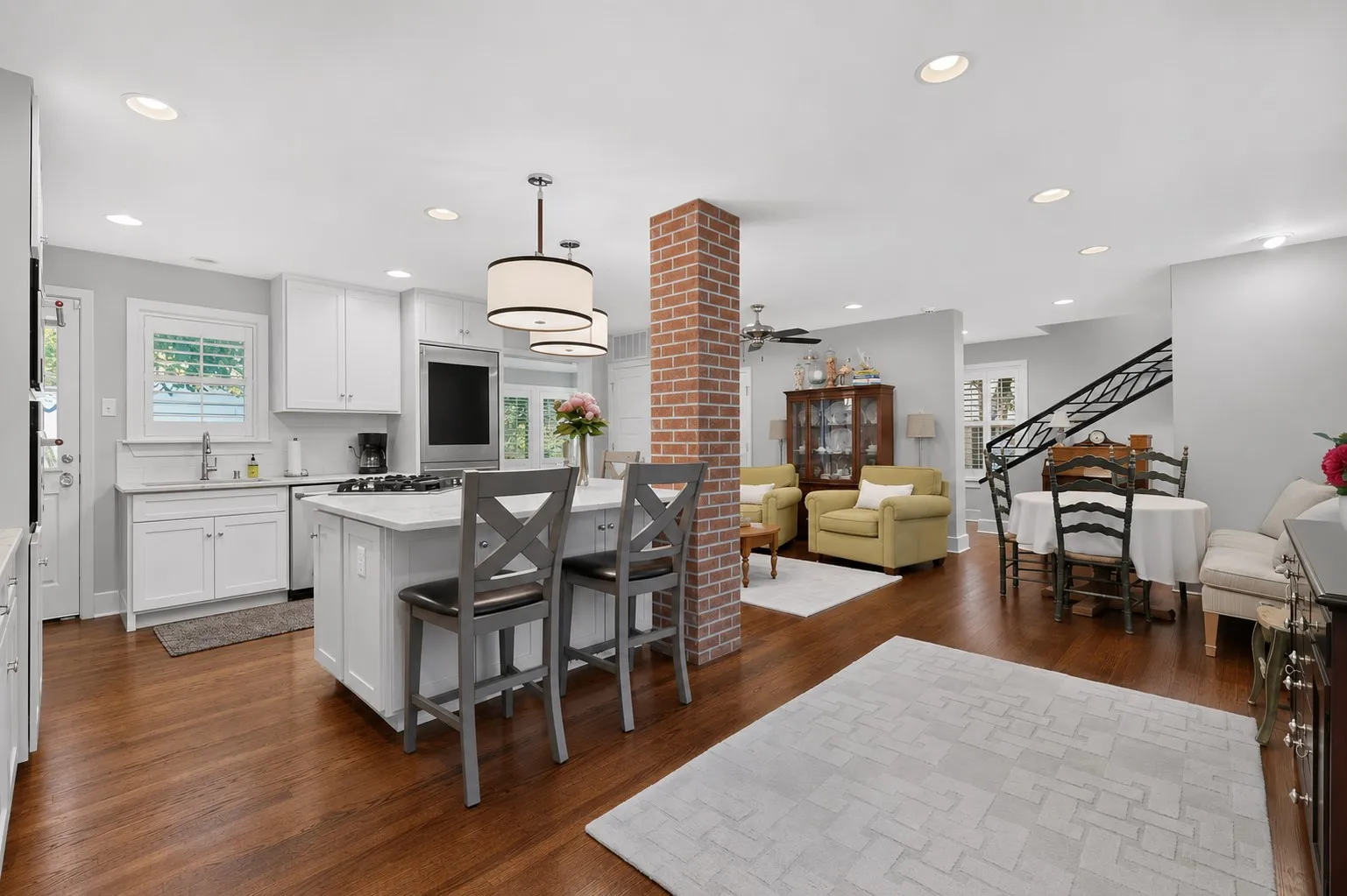 Hardwood flooring throughout, white cabinetry with integrated appliances, kitchen island with seating, recessed lighting, and a brick-faced structural column