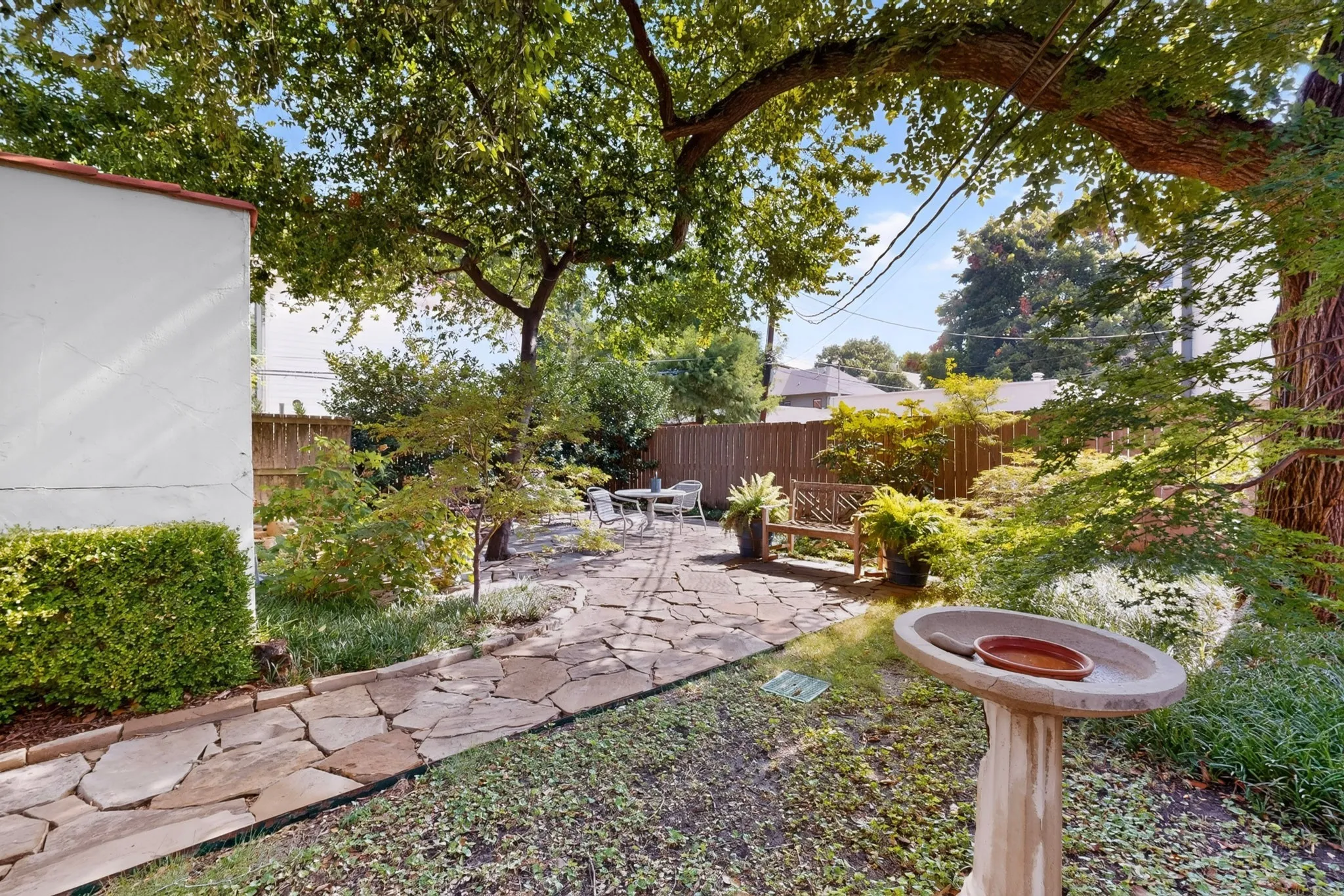Landscaped backyard featuring a stone patio, mature trees, and a privacy fence