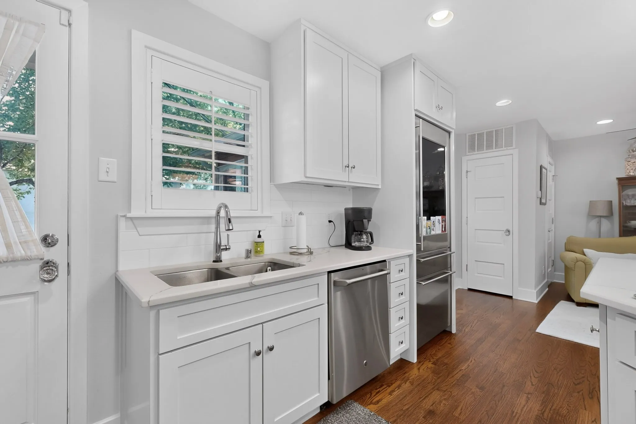 White cabinetry with brushed nickel hardware, stainless steel appliances, dual basin sink with gooseneck faucet, white subway tile backsplash, and wood-finish flooring