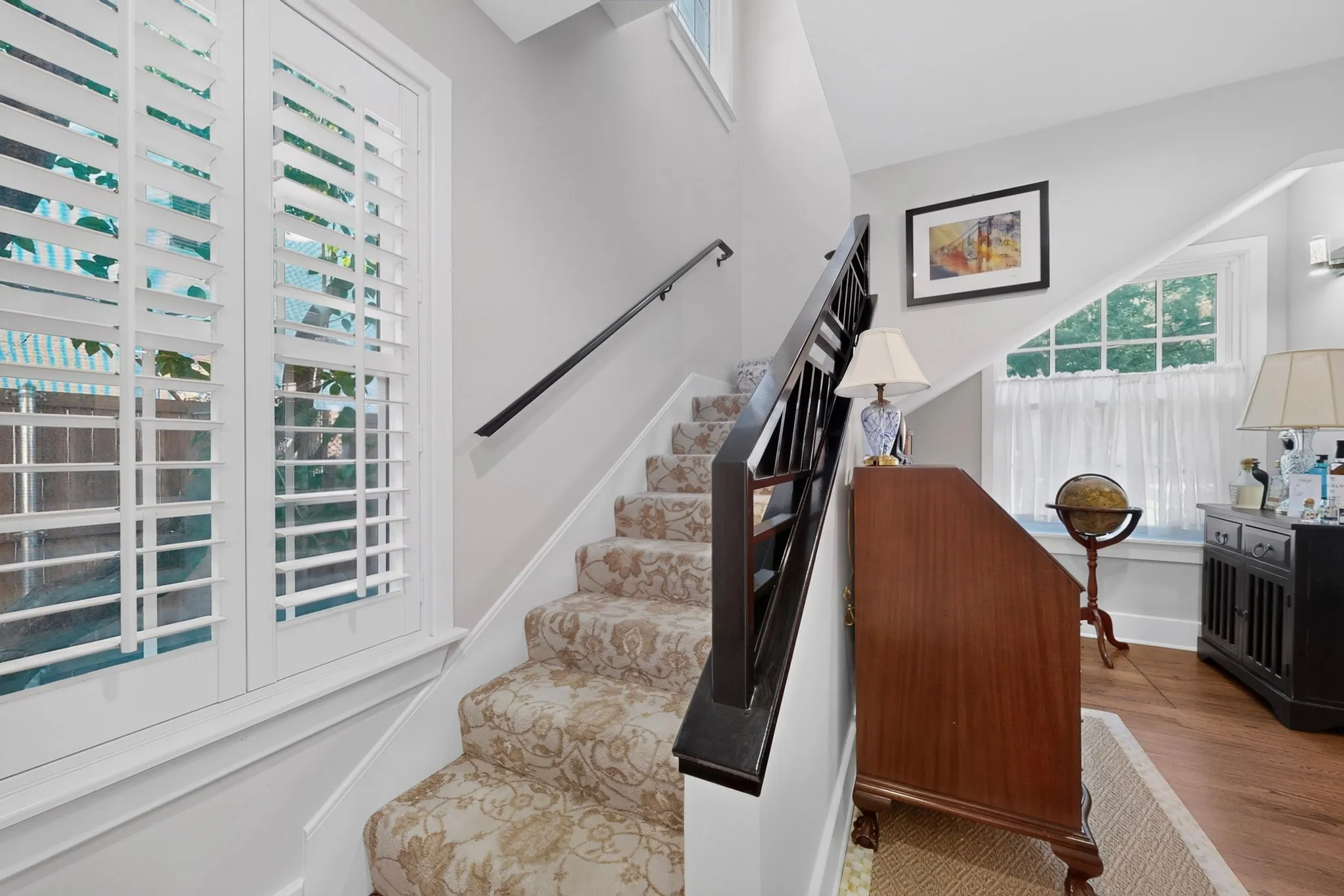 Staircase featuring patterned carpet, dark wood-finish handrail, and white plantation shutters