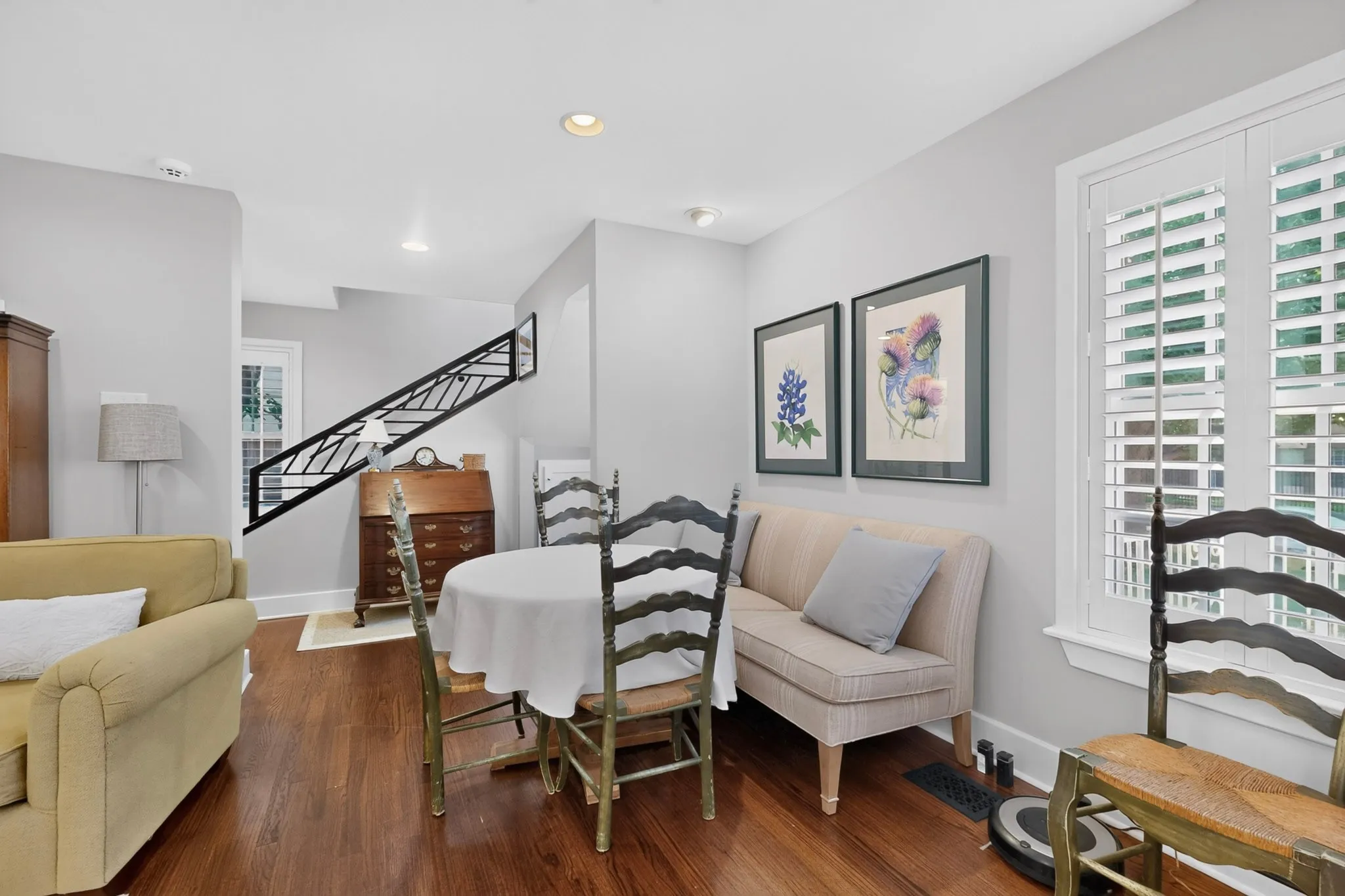 Rich wood-finish flooring, white plantation shutters, staircase with dark metal railing, recessed ceiling lighting, and neutral wall tones
