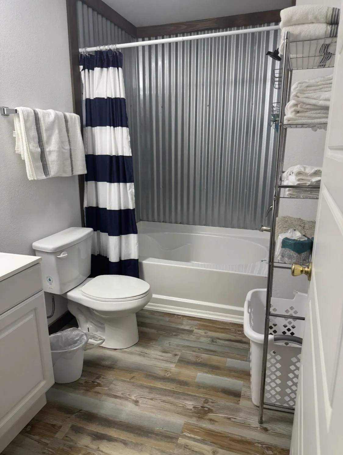 Tub and shower combination with corrugated metal surround, wood-finish flooring, and a white toilet