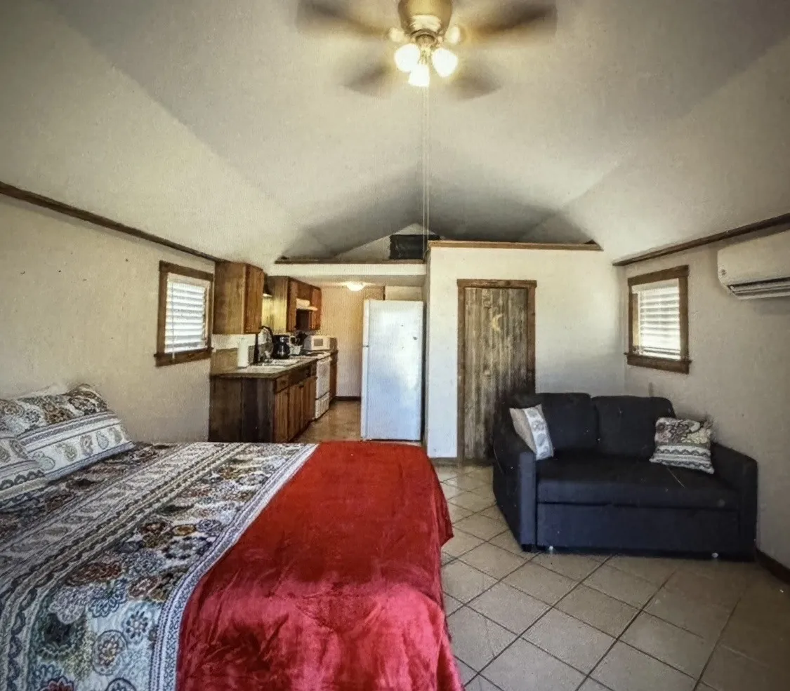 CABIN living space featuring a vaulted ceiling with a ceiling fan, a compact kitchen with wood-finish cabinetry, a window with horizontal blinds, and a built-in air conditioning unit