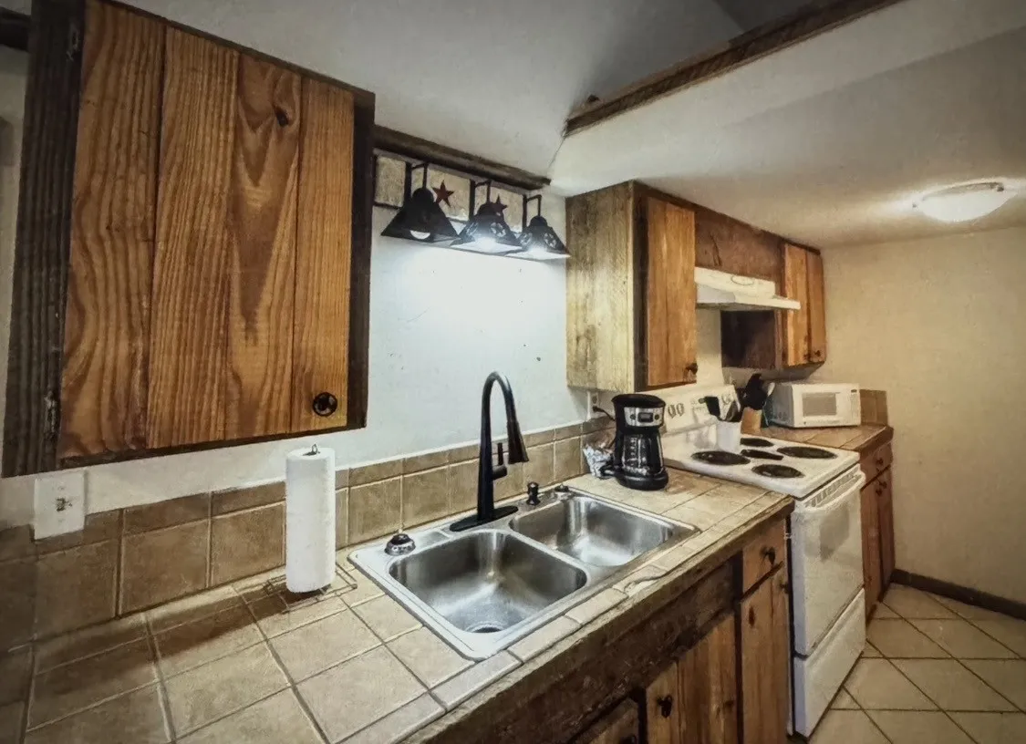 CABIN Kitchen featuring wood cabinetry, tile countertops, a double basin stainless steel sink with a gooseneck faucet, a white range, and a white range hood