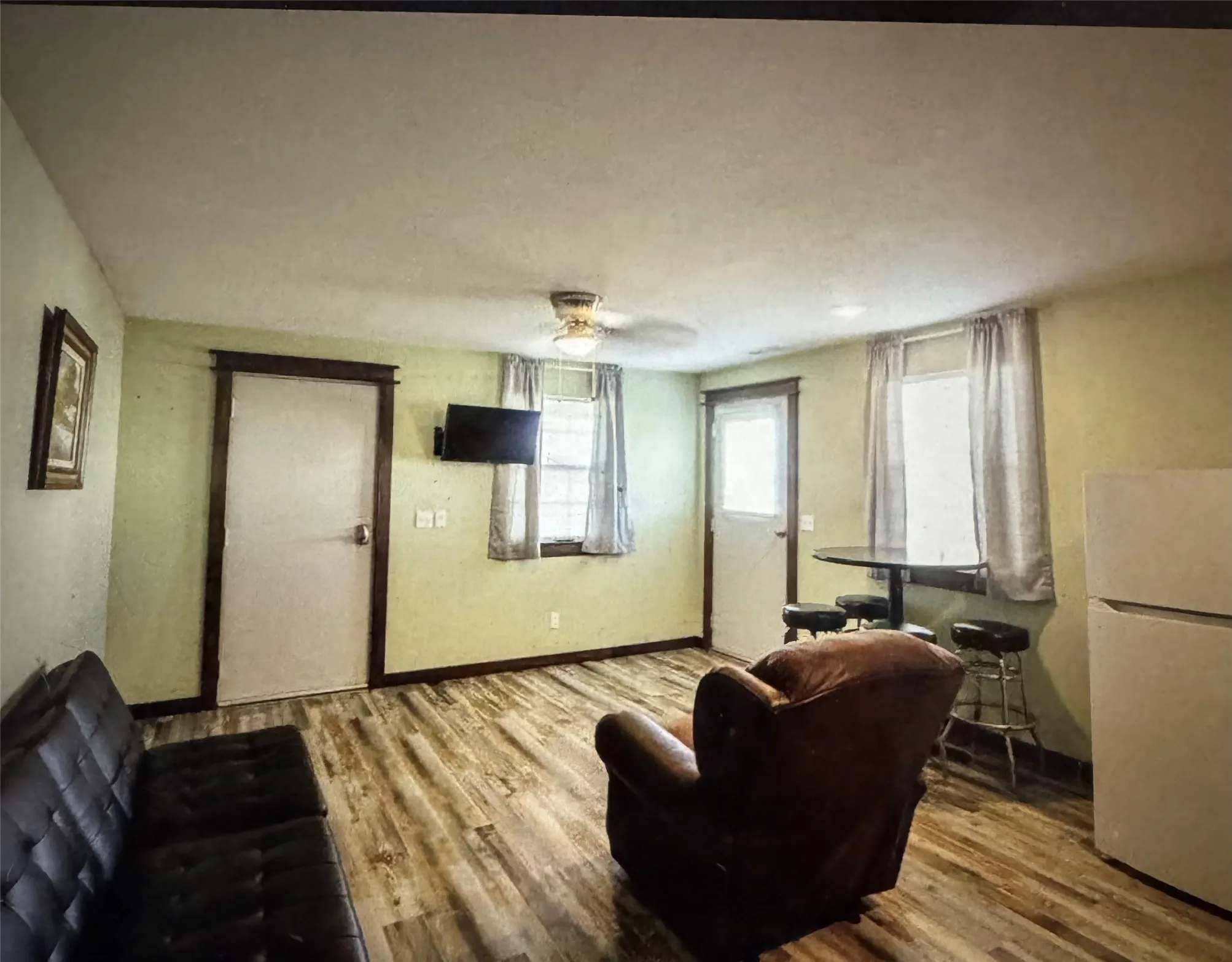 Suite Living Area Wood-finish flooring, two windows with trim, and a ceiling fan with integrated lighting