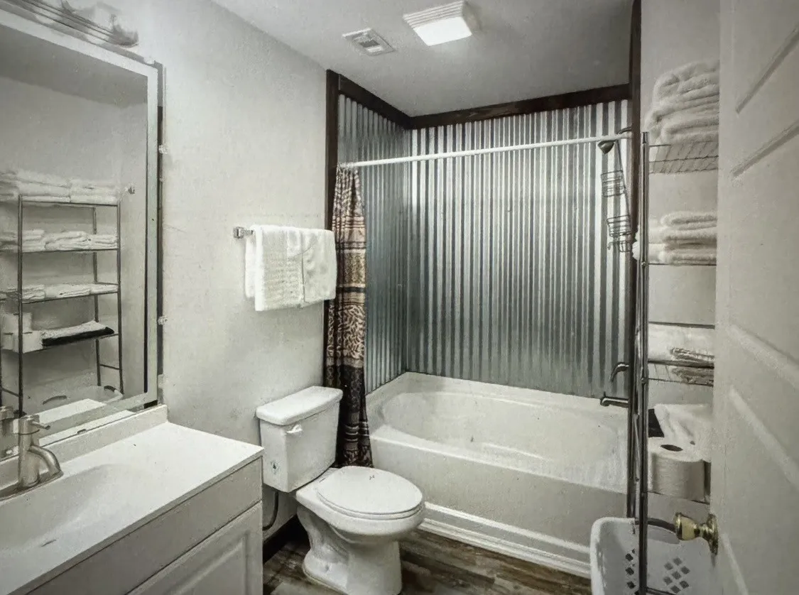 Bathroom featuring a vanity with an integrated sink, a commode, and a tub with a corrugated metal surround