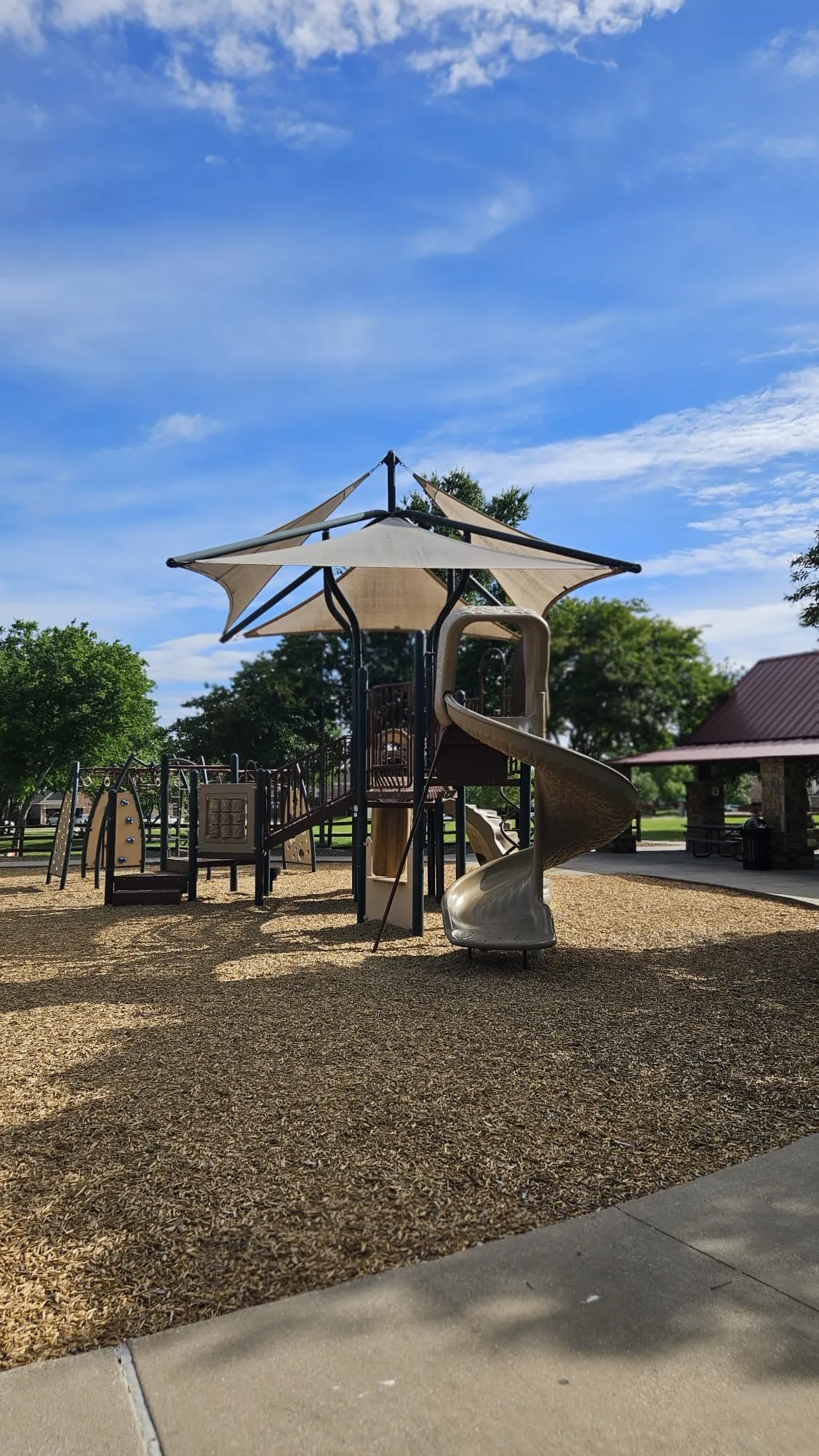 Playground structure with shade canopy, spiral slide, and wood chip ground covering