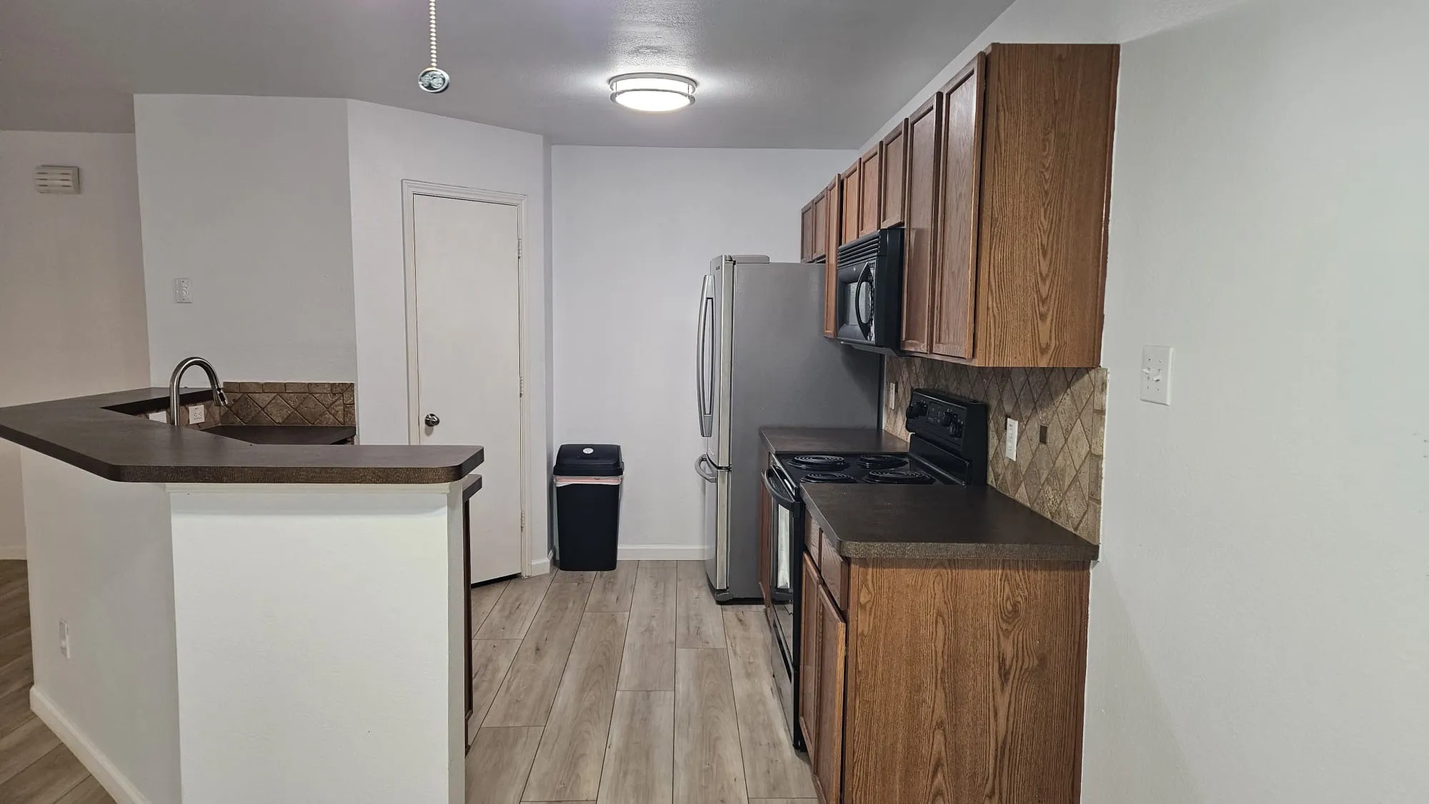 Kitchen featuring wood-finish cabinetry, stainless steel refrigerator, black stove, and a tiled backsplash