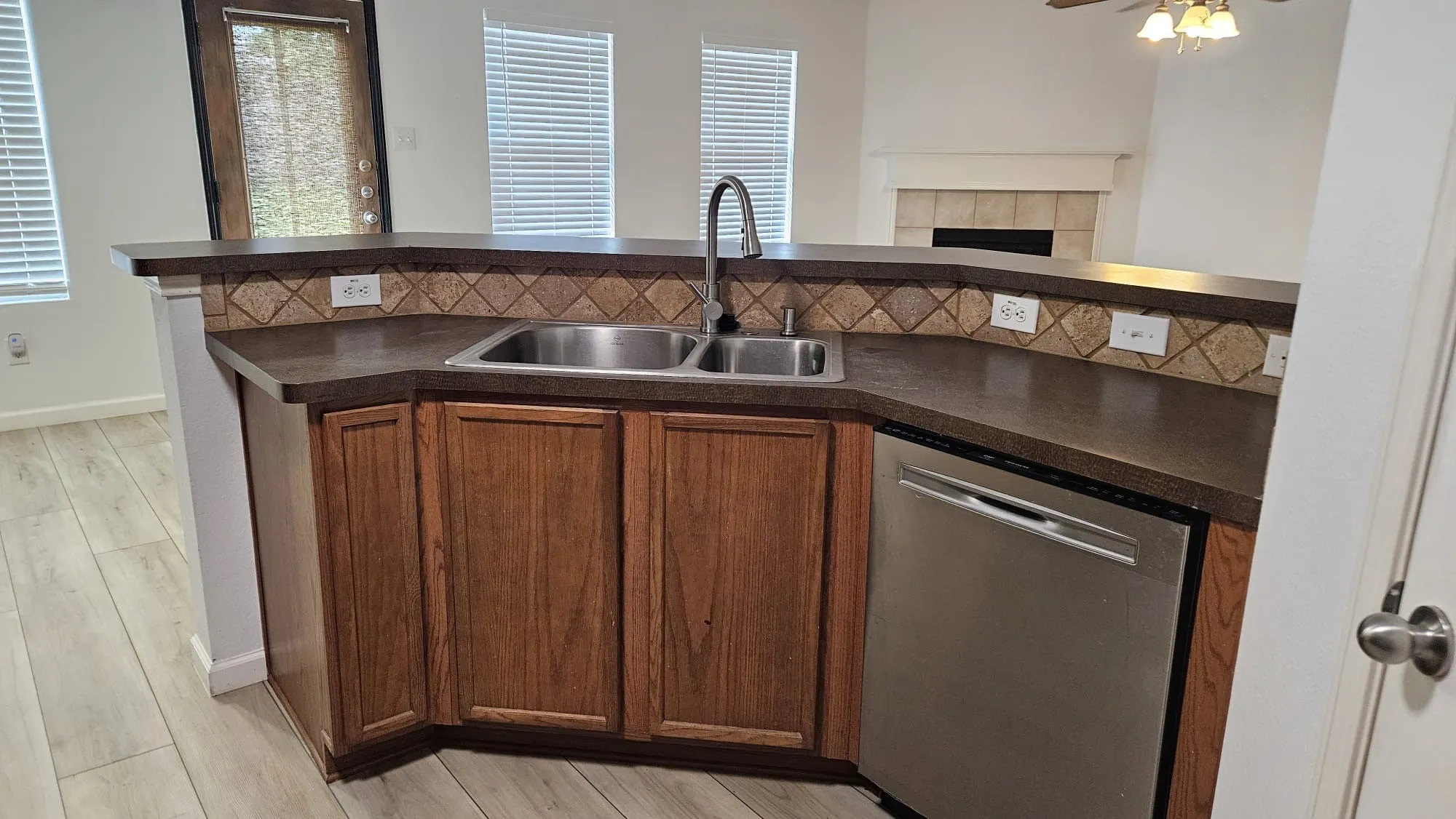 Kitchen island with wood-finish cabinetry, stainless steel double-basin sink, and a stainless steel dishwasher