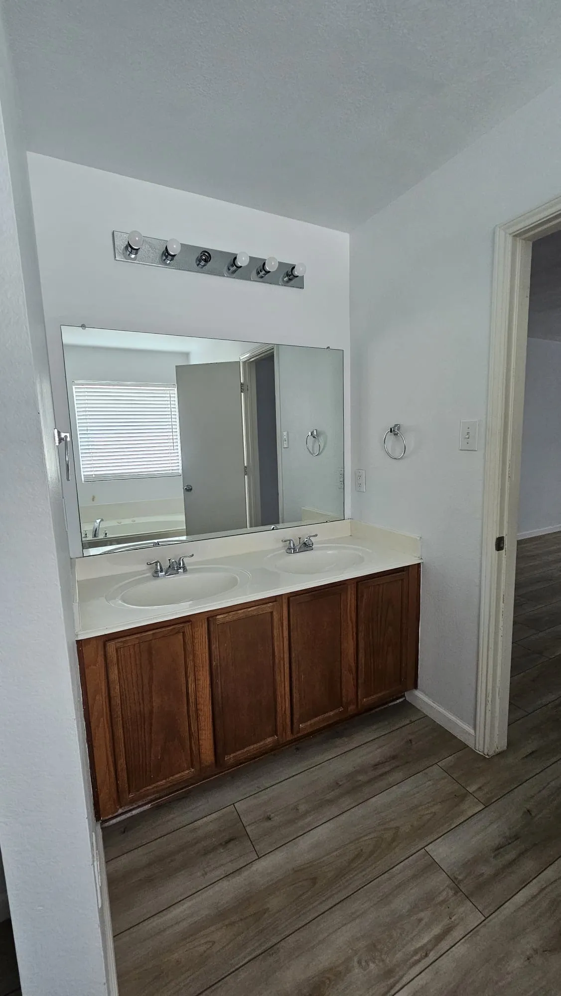 Dual sink vanity with wood-finish cabinetry, integrated countertop, and wood-finish flooring