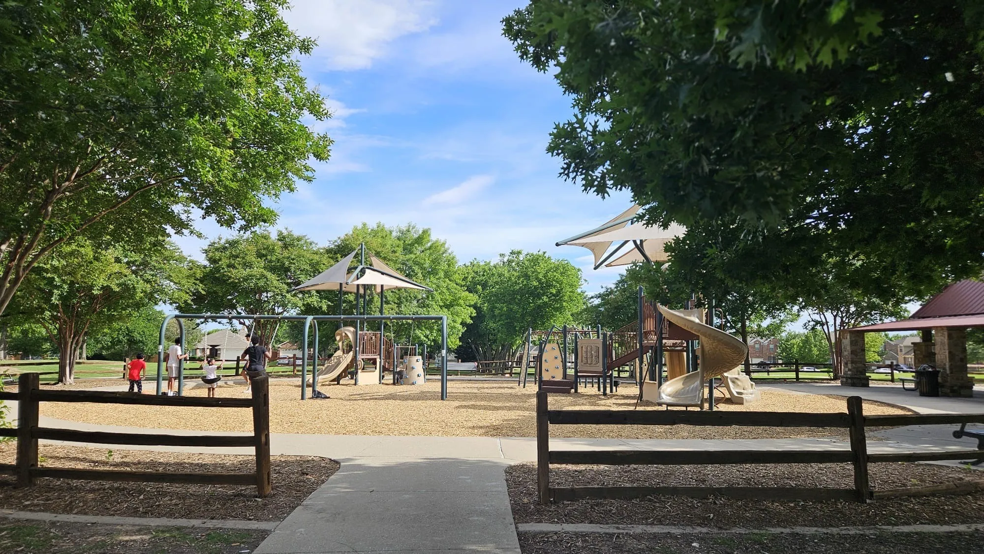 Community playground featuring multiple play structures, swings, and shade canopies