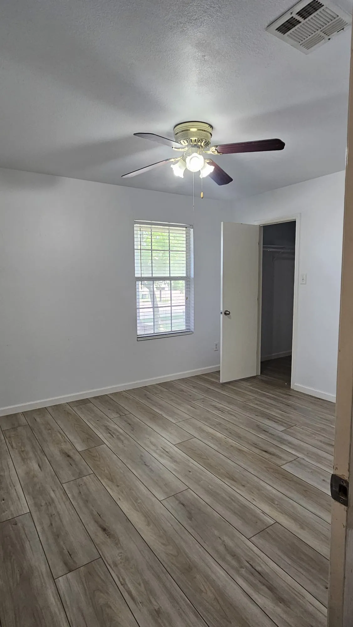 Wood-finish flooring, ceiling fan with integrated lighting, window with blinds, and white walls