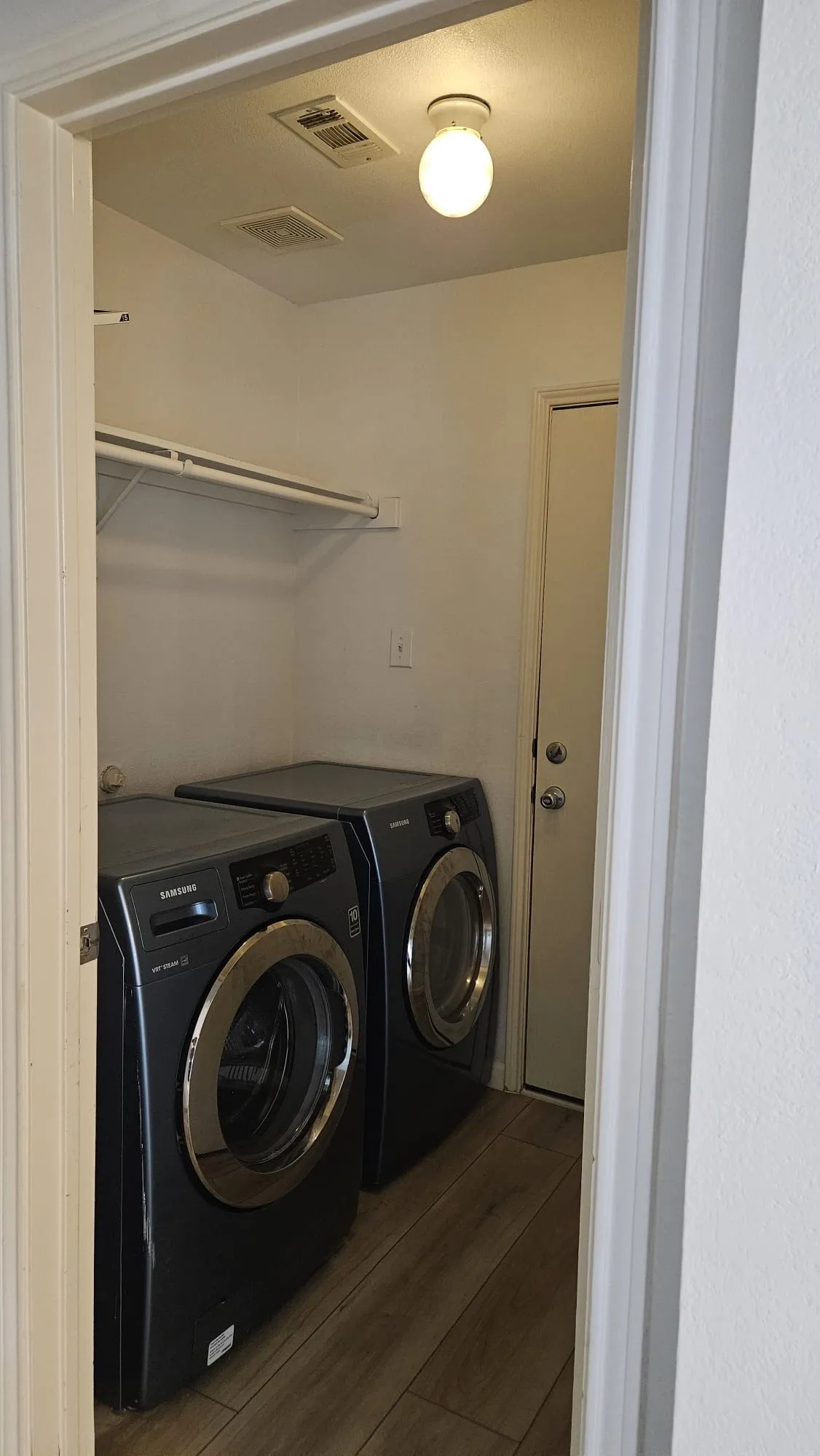 Laundry area featuring wood-finish flooring, overhead shelving, and a ceiling-mounted light fixture