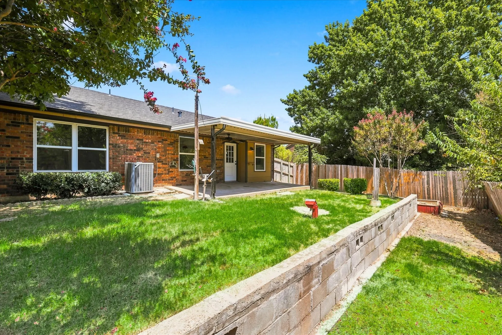 Brick exterior with a covered patio, a well-maintained lawn, and a wood privacy fence